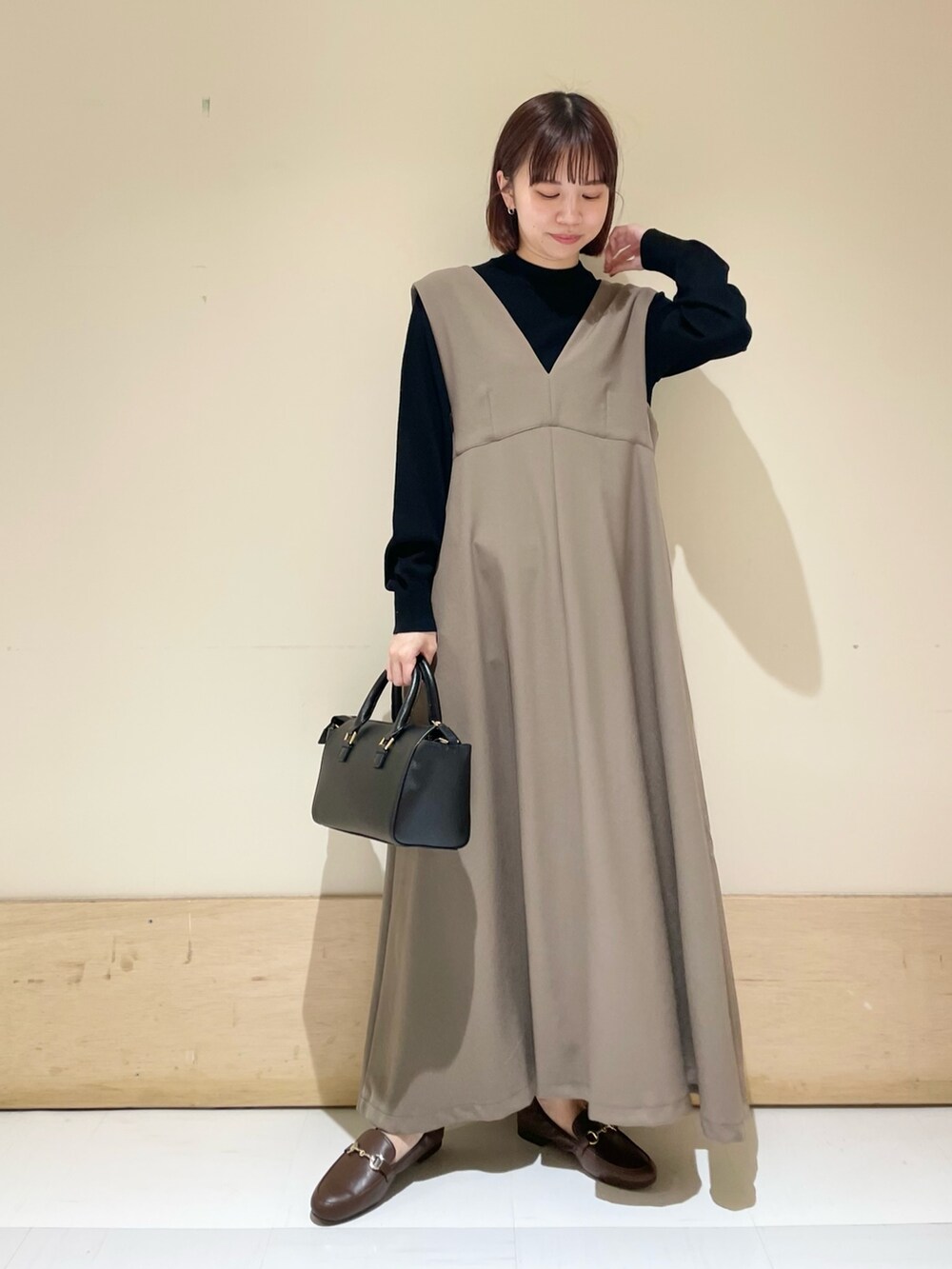 ベージュ系のワンピース、ブラック系のニット/セーター、ブラウン系のローファーを着用したレディースの冬コーディネートの2枚目の写真