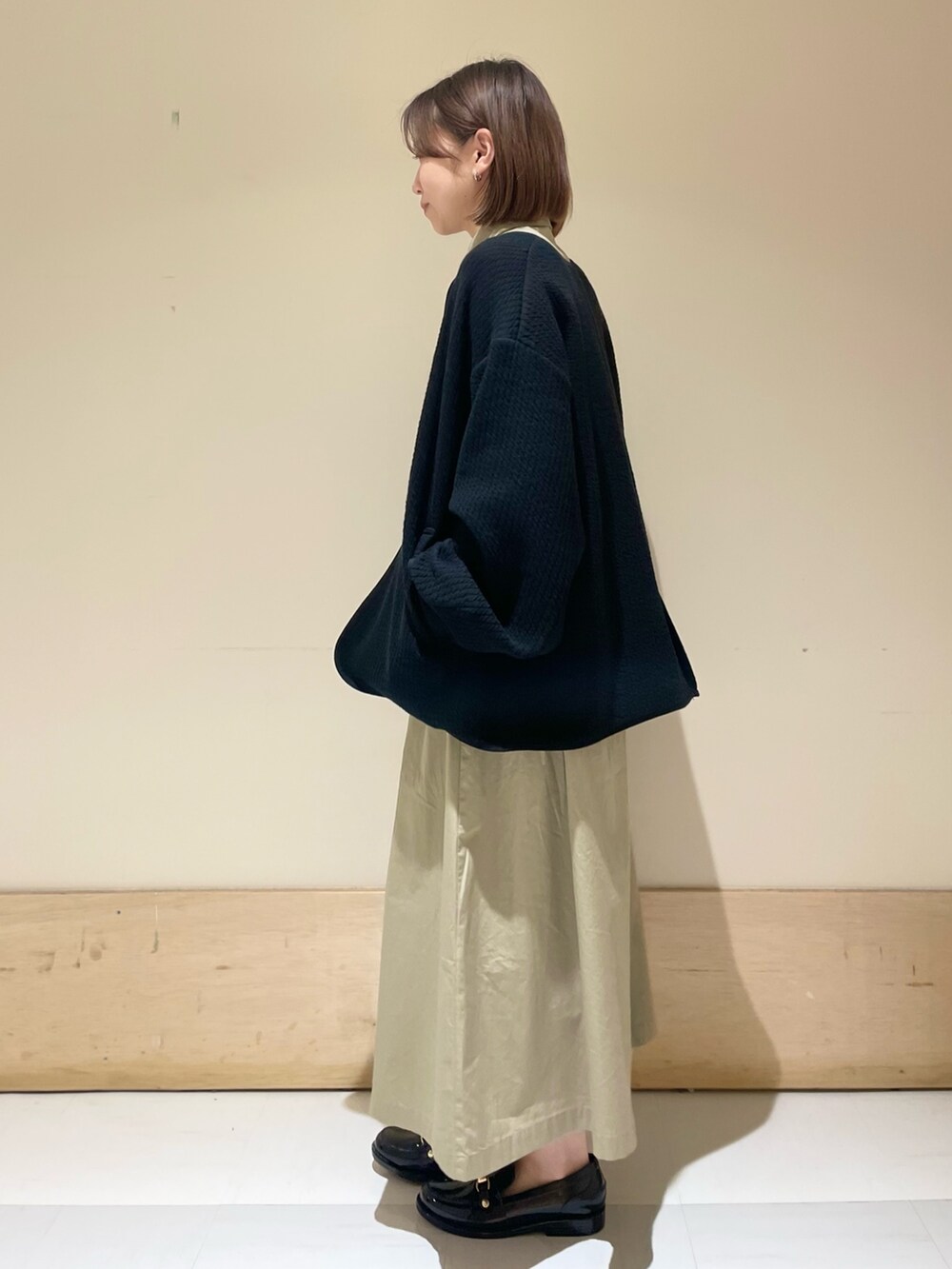 グレー系のショルダーバッグ、ブラック系のノーカラージャケット、ベージュ系のワンピースを着用したレディースの秋コーディネートの4枚目の写真