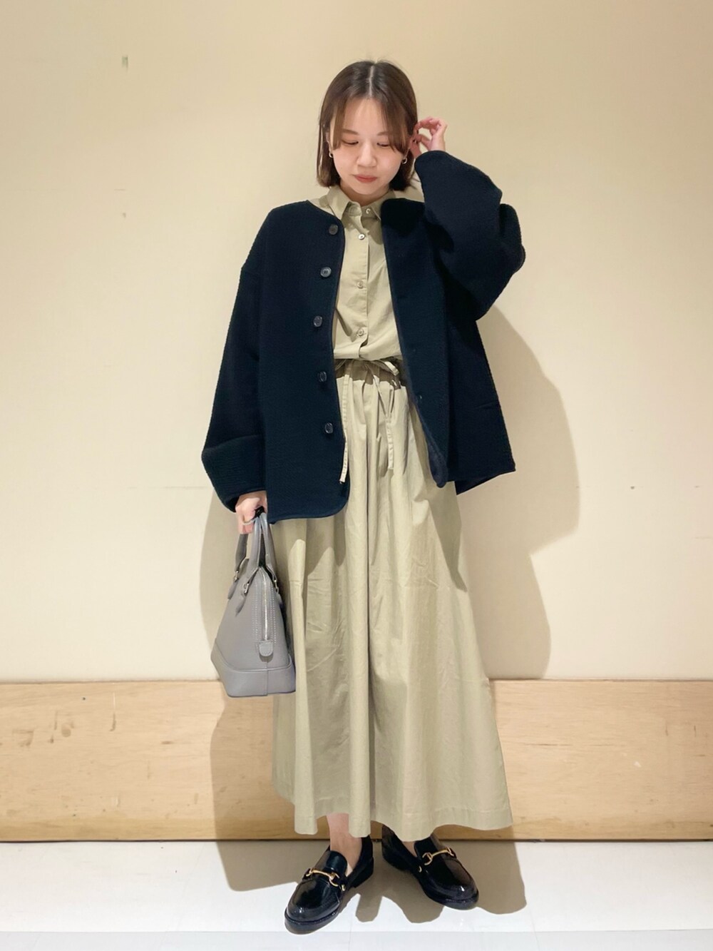 グレー系のショルダーバッグ、ブラック系のノーカラージャケット、ベージュ系のワンピースを着用したレディースの秋コーディネートの2枚目の写真