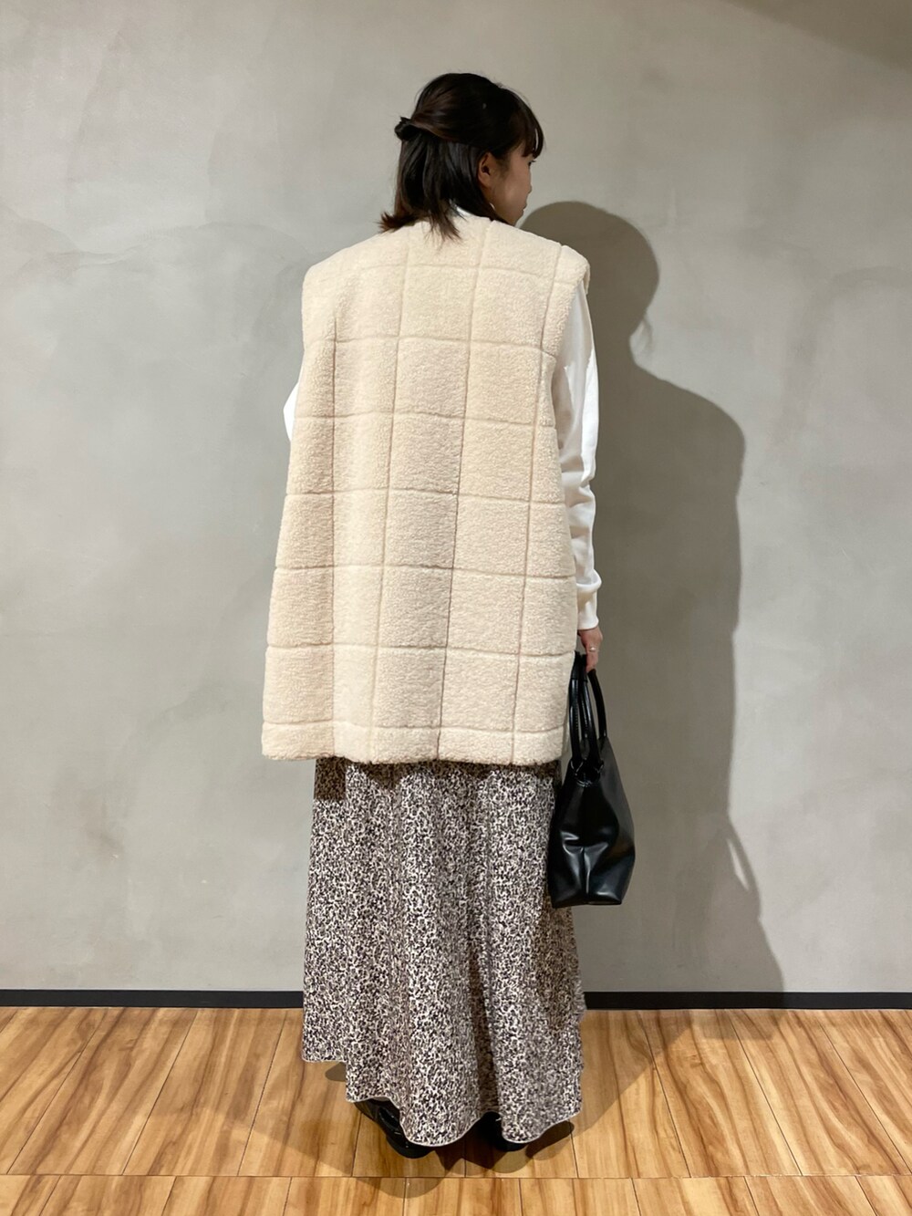 ブラック系のハンドバッグ、ベージュ系のスカート、ホワイト系のベストを着用したレディースの秋コーディネートの5枚目の写真