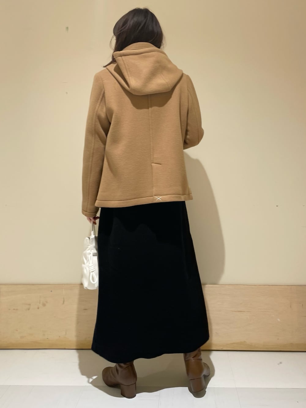 イエロー系のピーコート、ブラック系のワンピース、ブラウン系のブーツを着用したレディースの冬コーディネートの3枚目の写真