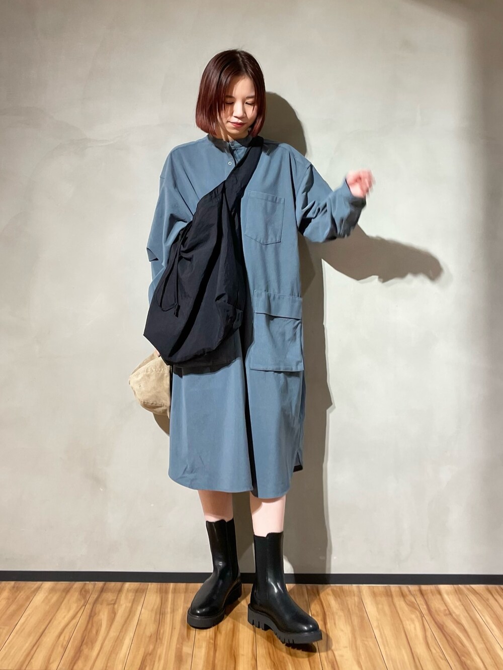 グレー系のワンピース、ブラック系のブーツ、ブラック系のショルダーバッグを着用したレディースの秋コーディネートの2枚目の写真