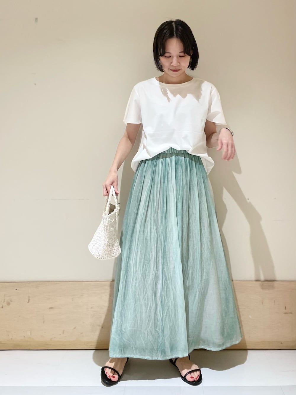 ブルー系のスカート、ホワイト系のハンドバッグ、ブラック系のサンダルを着用したレディースの夏コーディネートの2枚目の写真