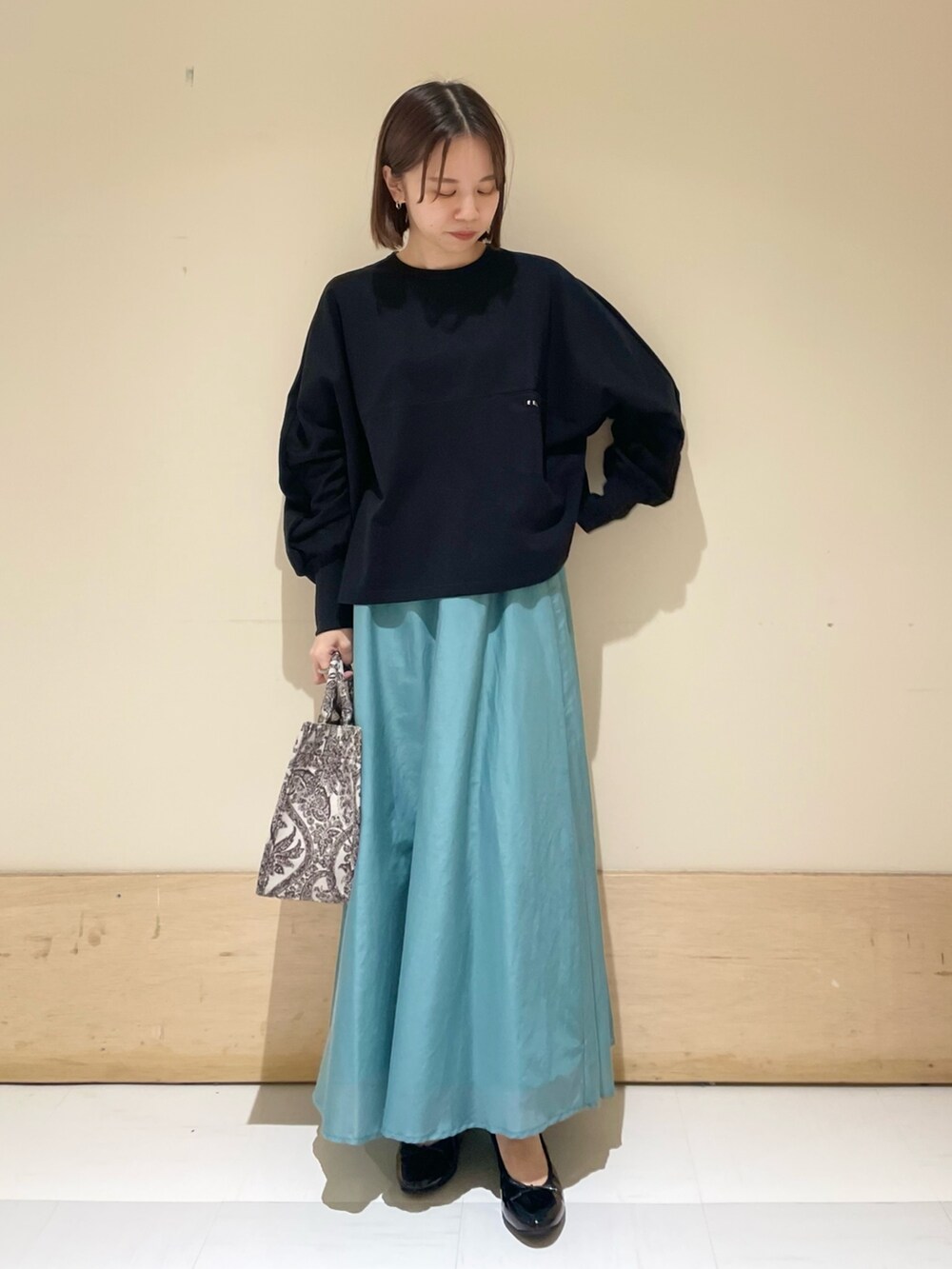 ブラック系のTシャツ/カットソー、グリーン系のスカート、ブラウン系のトートバッグを着用したレディースの秋コーディネートの2枚目の写真