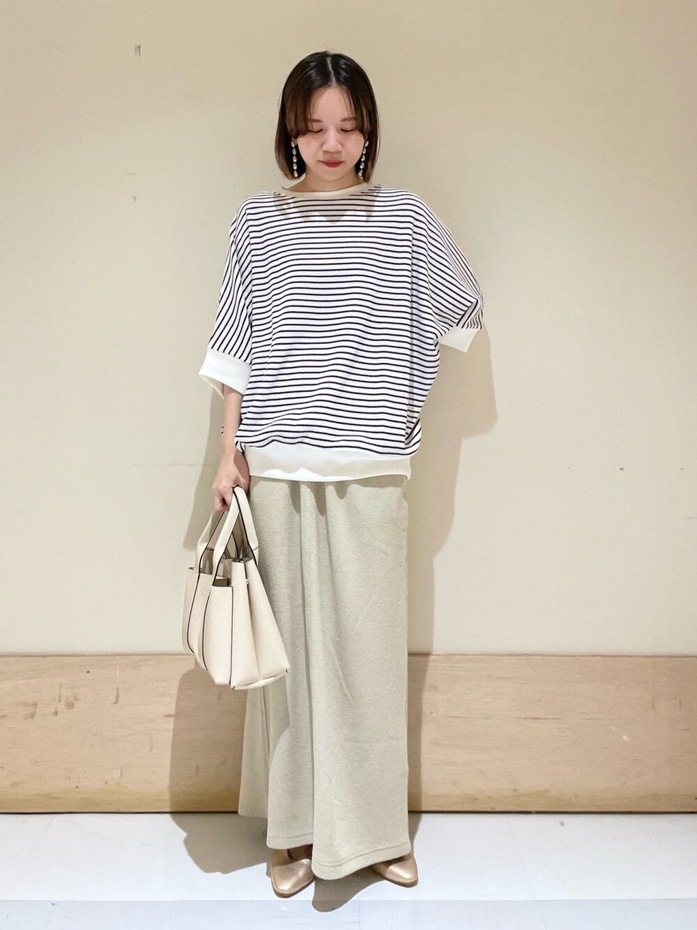 ベージュ系のスカート、ホワイト系のTシャツ/カットソー、ホワイト系のトートバッグを着用したレディースの秋コーディネートの2枚目の写真