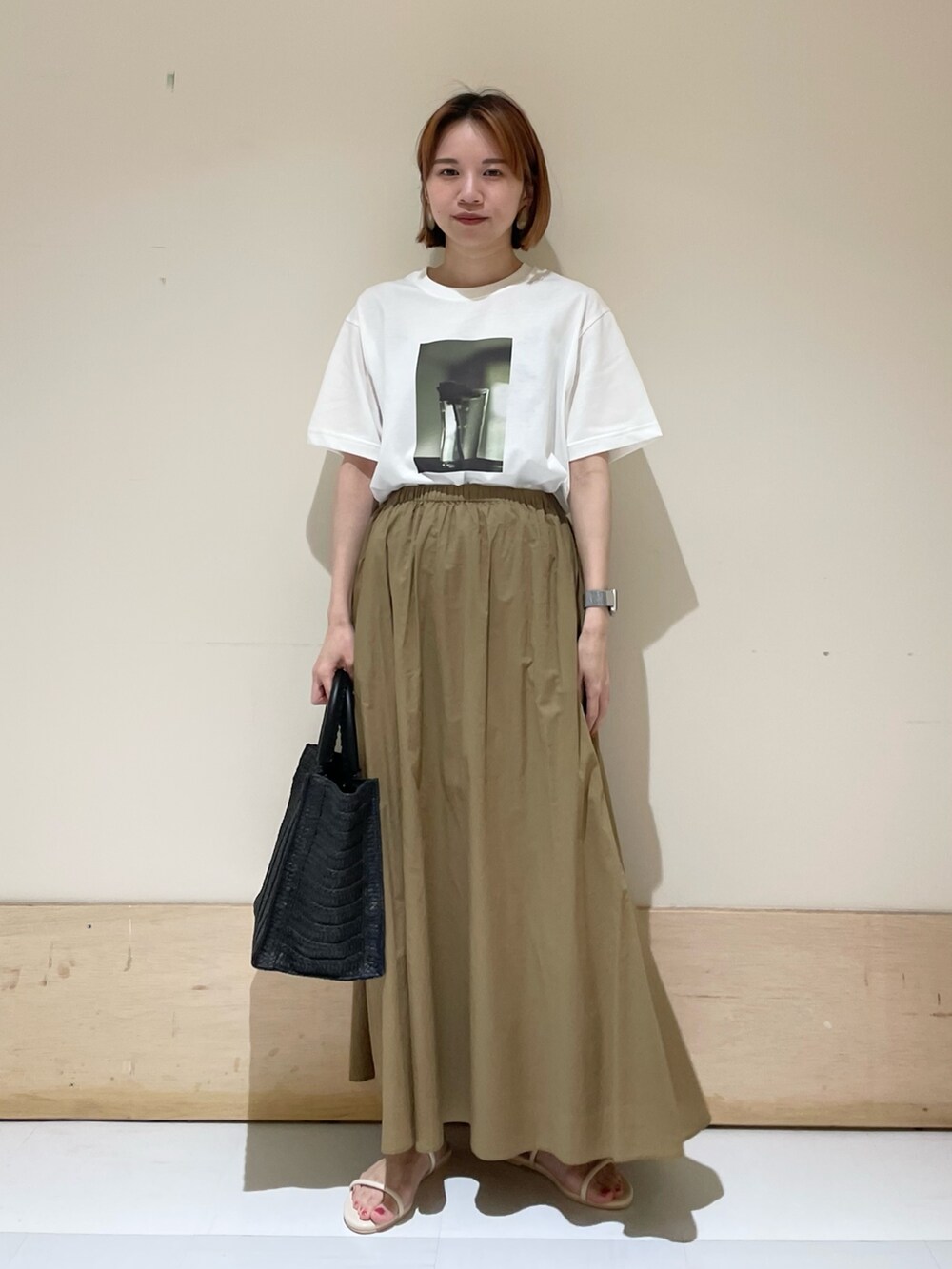 ベージュ系のスカート、ホワイト系のサンダル、ブラック系のトートバッグを着用したレディースの夏コーディネートの2枚目の写真