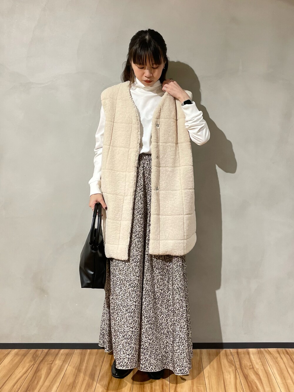 ブラック系のハンドバッグ、ベージュ系のスカート、ホワイト系のベストを着用したレディースの秋コーディネートの2枚目の写真
