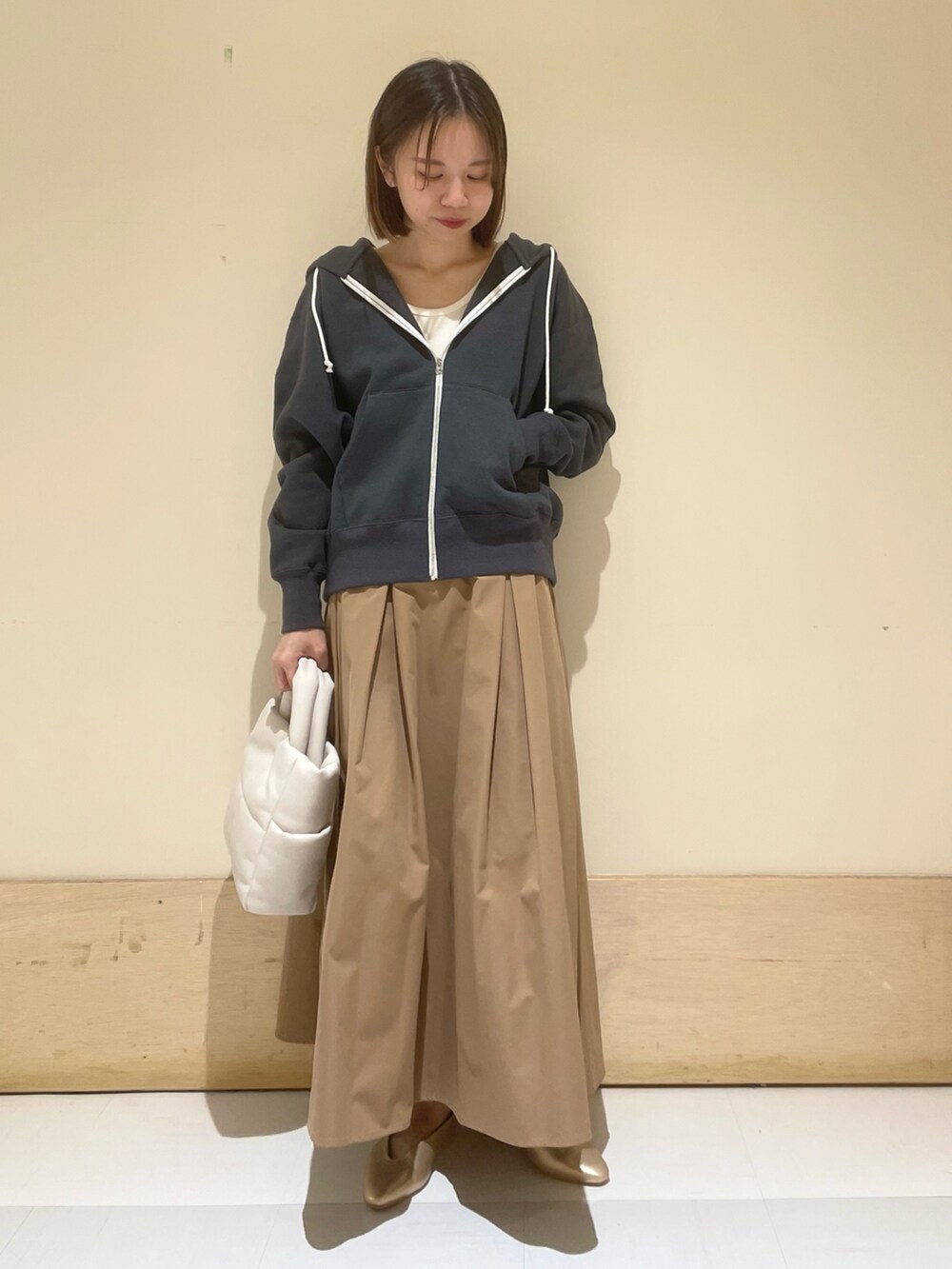 ゴールド系のパンプス、ホワイト系のトートバッグ、ベージュ系のスカートを着用したレディースの秋コーディネートの2枚目の写真