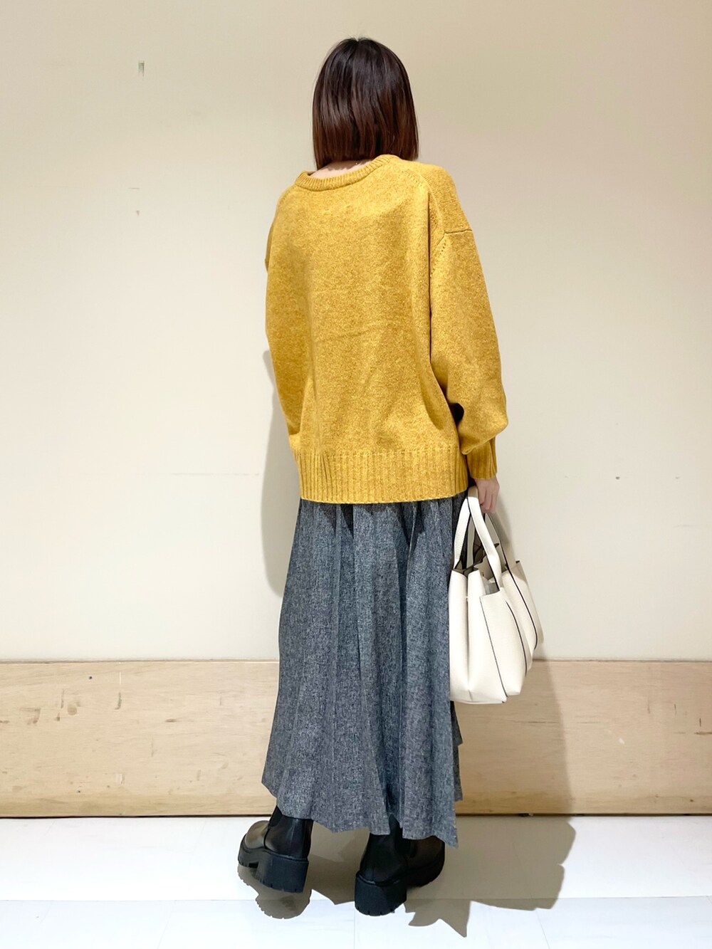 イエロー系のニット/セーター、ブルー系のスカート、ブラック系のブーツを着用したレディースの冬コーディネートの7枚目の写真