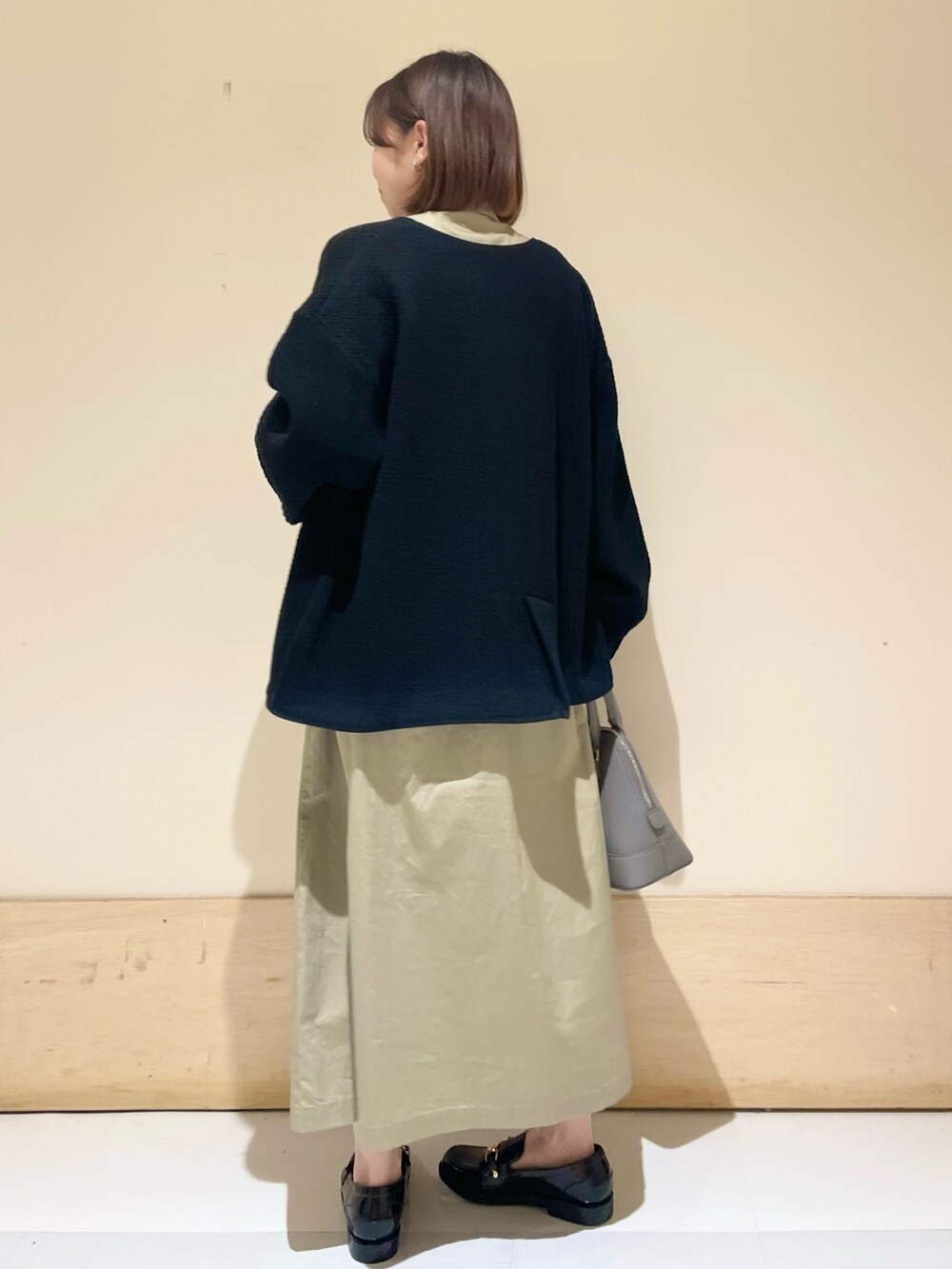 グレー系のショルダーバッグ、ブラック系のノーカラージャケット、ベージュ系のワンピースを着用したレディースの秋コーディネートの5枚目の写真