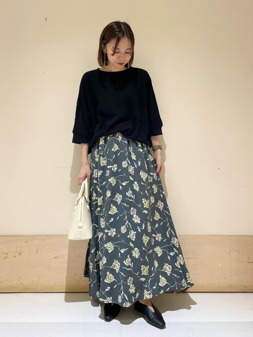 グレー系のスカート、ホワイト系のショルダーバッグ、ブラック系のパンプスを着用したレディースの秋コーディネートの2枚目の写真