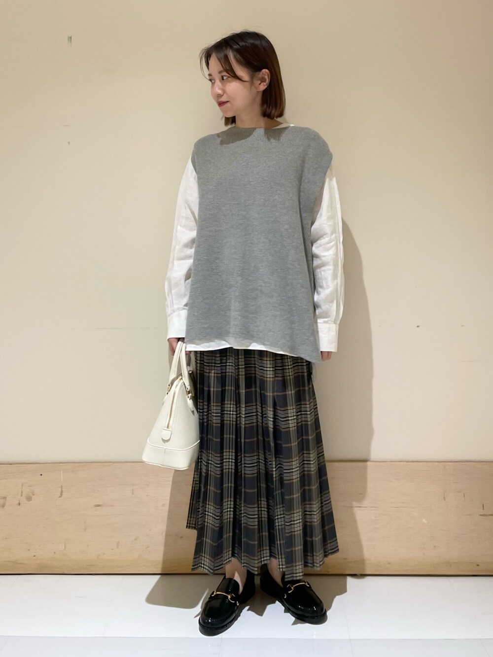グレー系のベスト、ホワイト系のTシャツ/カットソー、ブラック系のレインシューズを着用したレディースの秋コーディネートの3枚目の写真