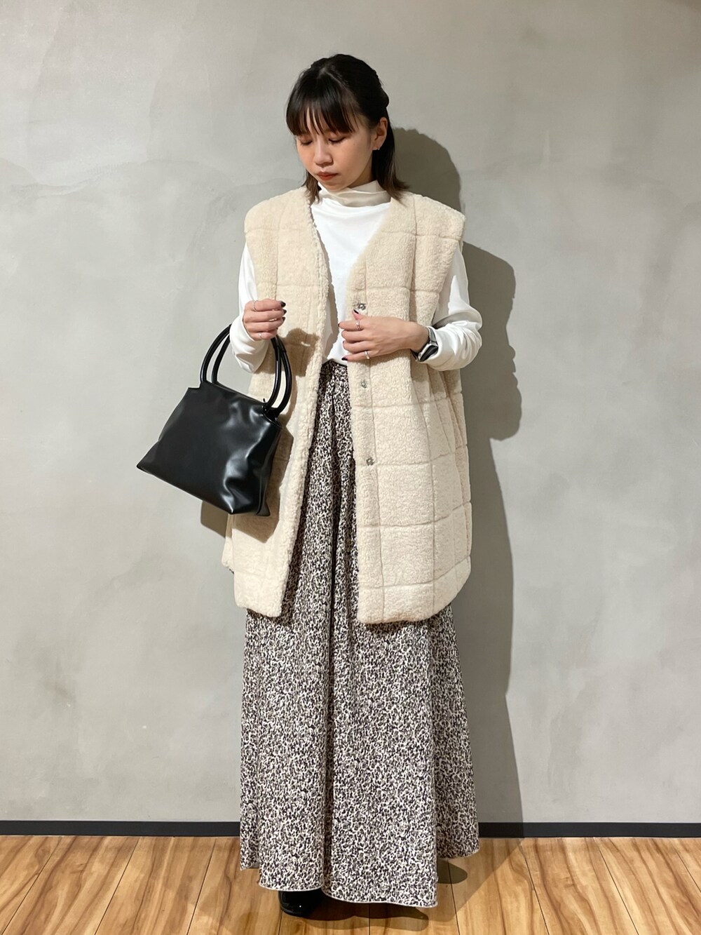 ブラック系のハンドバッグ、ベージュ系のスカート、ホワイト系のベストを着用したレディースの秋コーディネートの3枚目の写真