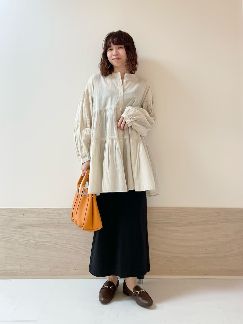 ブラック系のスカート、ホワイト系のチュニックを着用したレディースの春コーディネートの2枚目の写真