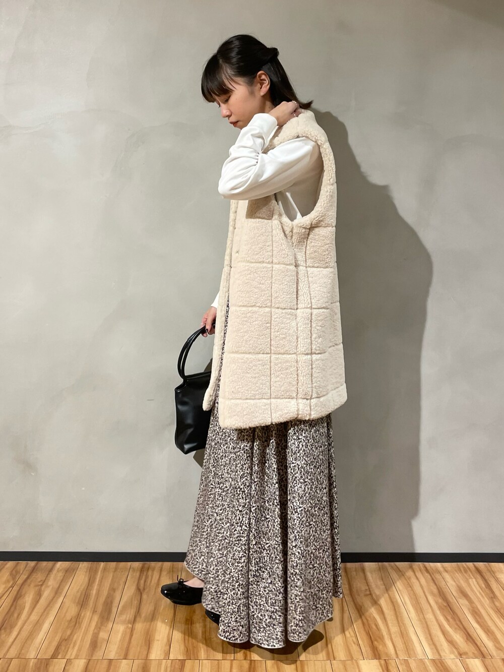 ブラック系のハンドバッグ、ベージュ系のスカート、ホワイト系のベストを着用したレディースの秋コーディネートの4枚目の写真