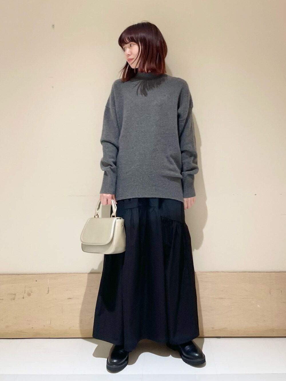 ブラック系のスカート、ゴールド系のショルダーバッグ、ブラック系のブーツを着用したレディースの冬コーディネートの2枚目の写真