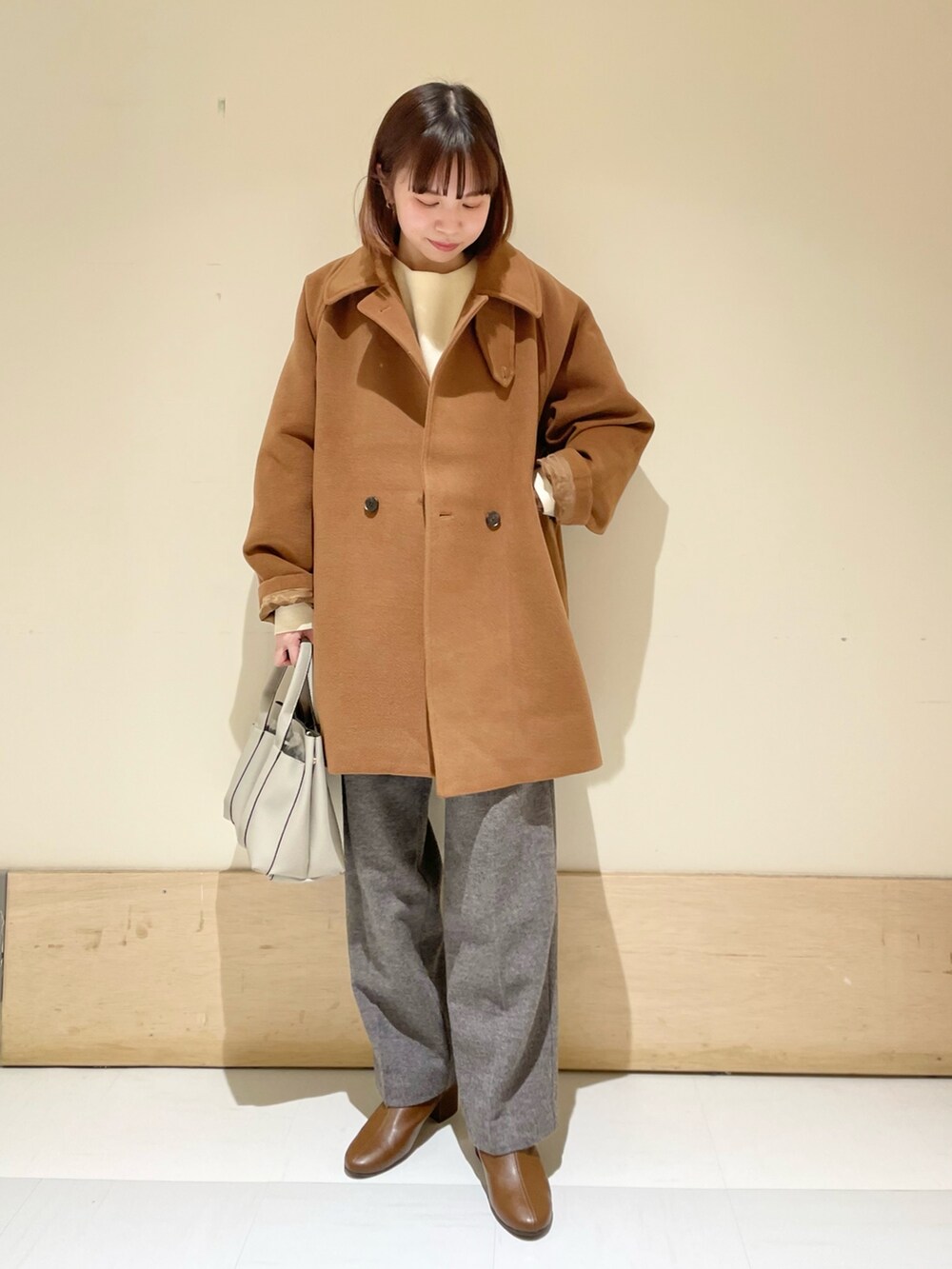 イエロー系のピーコート、ホワイト系のニット/セーター、グレー系のその他パンツを着用したレディースの冬コーディネートの2枚目の写真