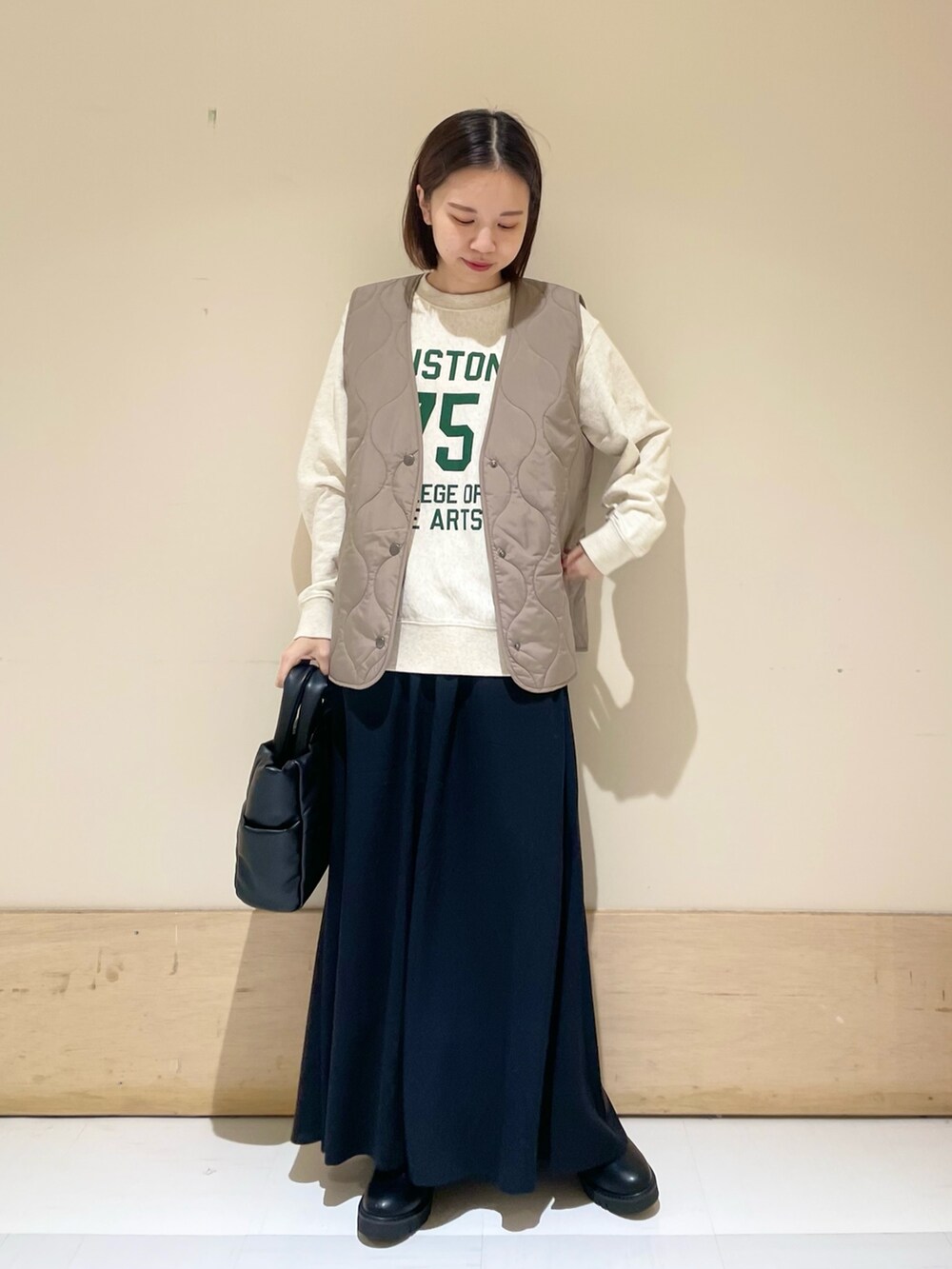 ブラック系のスカート、ブラック系のブーツ、ブラウン系のダウンベストを着用したレディースの秋コーディネートの2枚目の写真