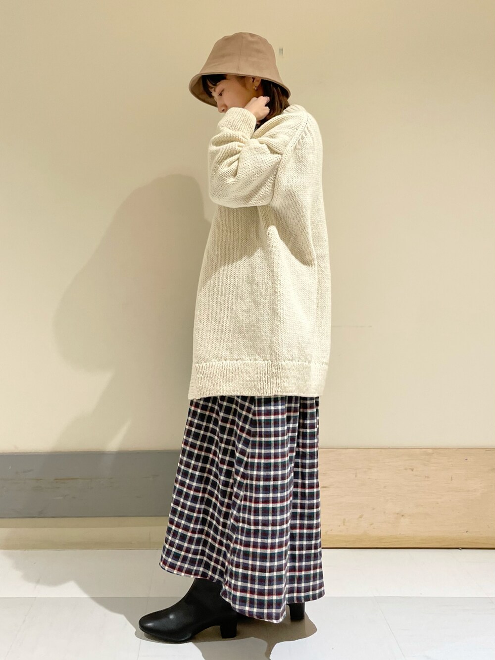 ブラウン系のワンピース、ホワイト系のカーディガン/ボレロ、ブラック系のブーツを着用したレディースの秋コーディネートの2枚目の写真