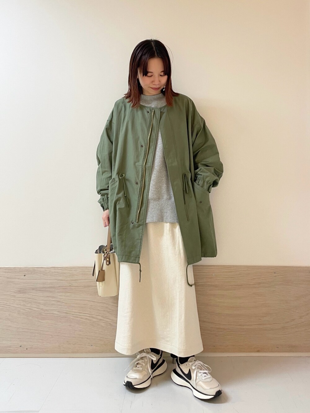 グリーン系のモッズコート、グレー系のTシャツ/カットソー、ホワイト系のスカートを着用したレディースの春コーディネートの2枚目の写真