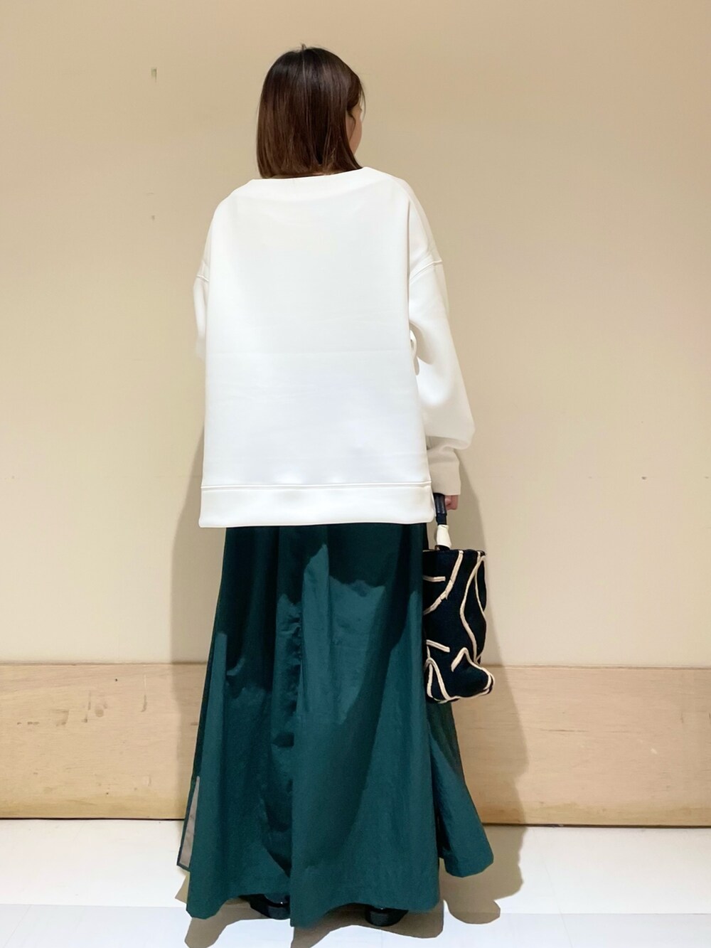 ブラック系のショルダーバッグ、グリーン系のスカート、ブラック系のレインシューズを着用したレディースの秋コーディネートの5枚目の写真