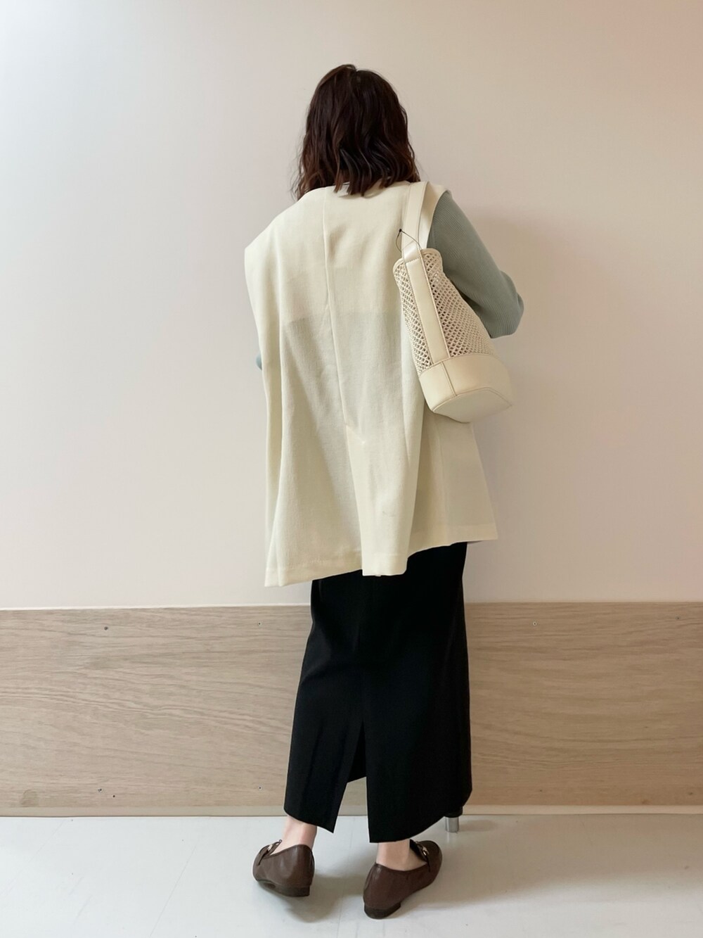 グリーン系のニット/セーター、ホワイト系のその他アウター、ブラック系のスカートを着用したレディースの春コーディネートの6枚目の写真