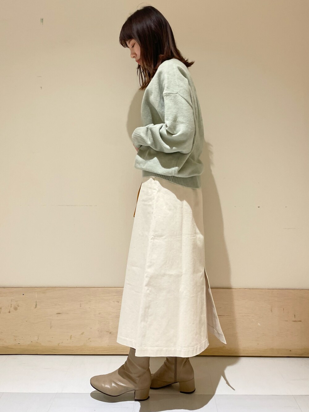 グリーン系のニット/セーター、イエロー系のショルダーバッグ、ホワイト系のスカートを着用したレディースの冬コーディネートの2枚目の写真