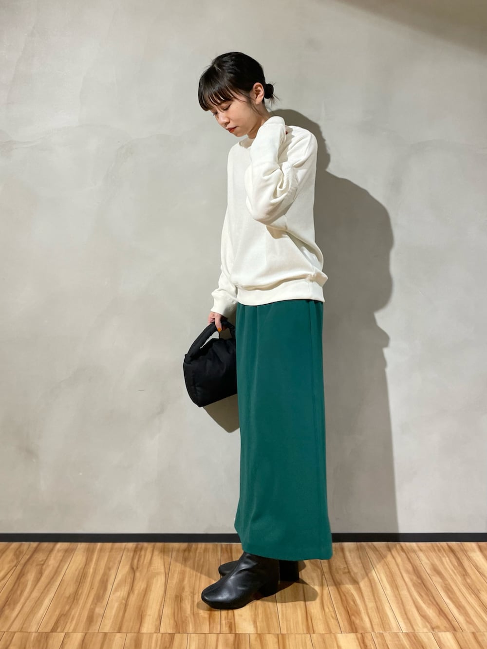 ブラック系のハンドバッグ、ホワイト系のTシャツ/カットソー、グリーン系のスカートを着用したレディースの秋コーディネートの2枚目の写真