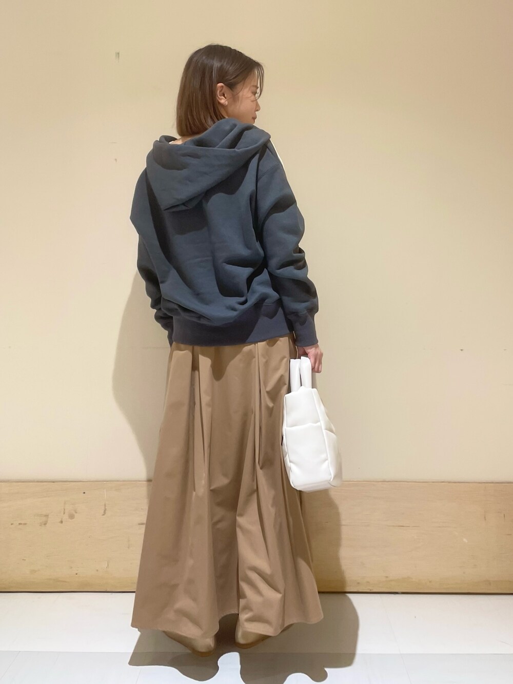 ゴールド系のパンプス、ホワイト系のトートバッグ、ベージュ系のスカートを着用したレディースの秋コーディネートの5枚目の写真