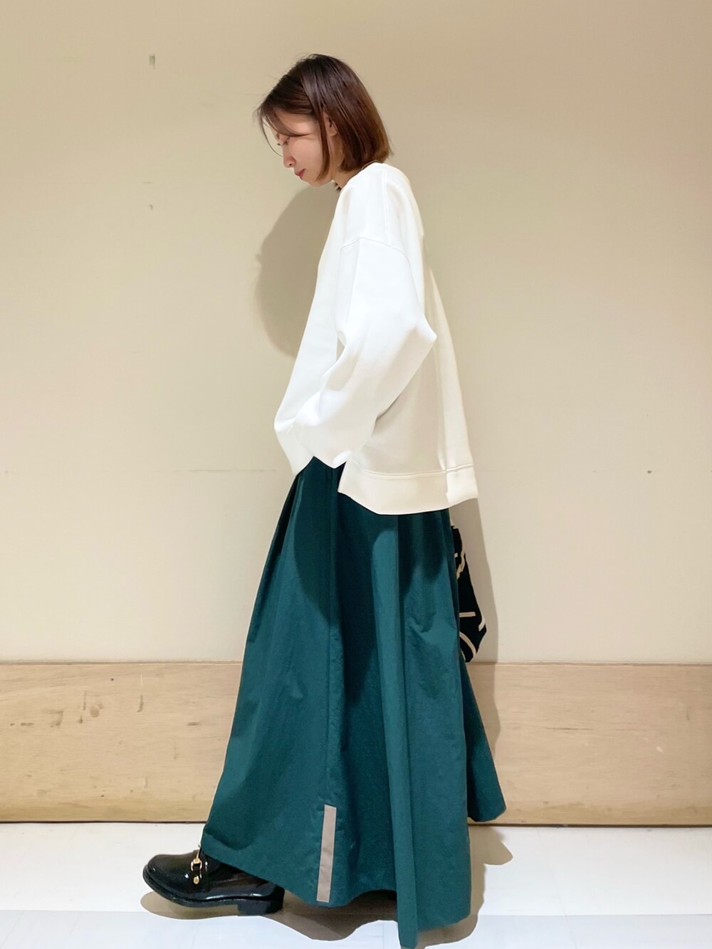 ブラック系のショルダーバッグ、グリーン系のスカート、ブラック系のレインシューズを着用したレディースの秋コーディネートの4枚目の写真