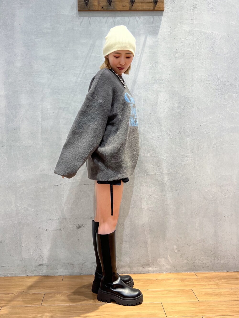 グレー系のニット/セーター、ブラック系のスカート、ブラック系のブーツを着用したレディースの秋コーディネートの2枚目の写真