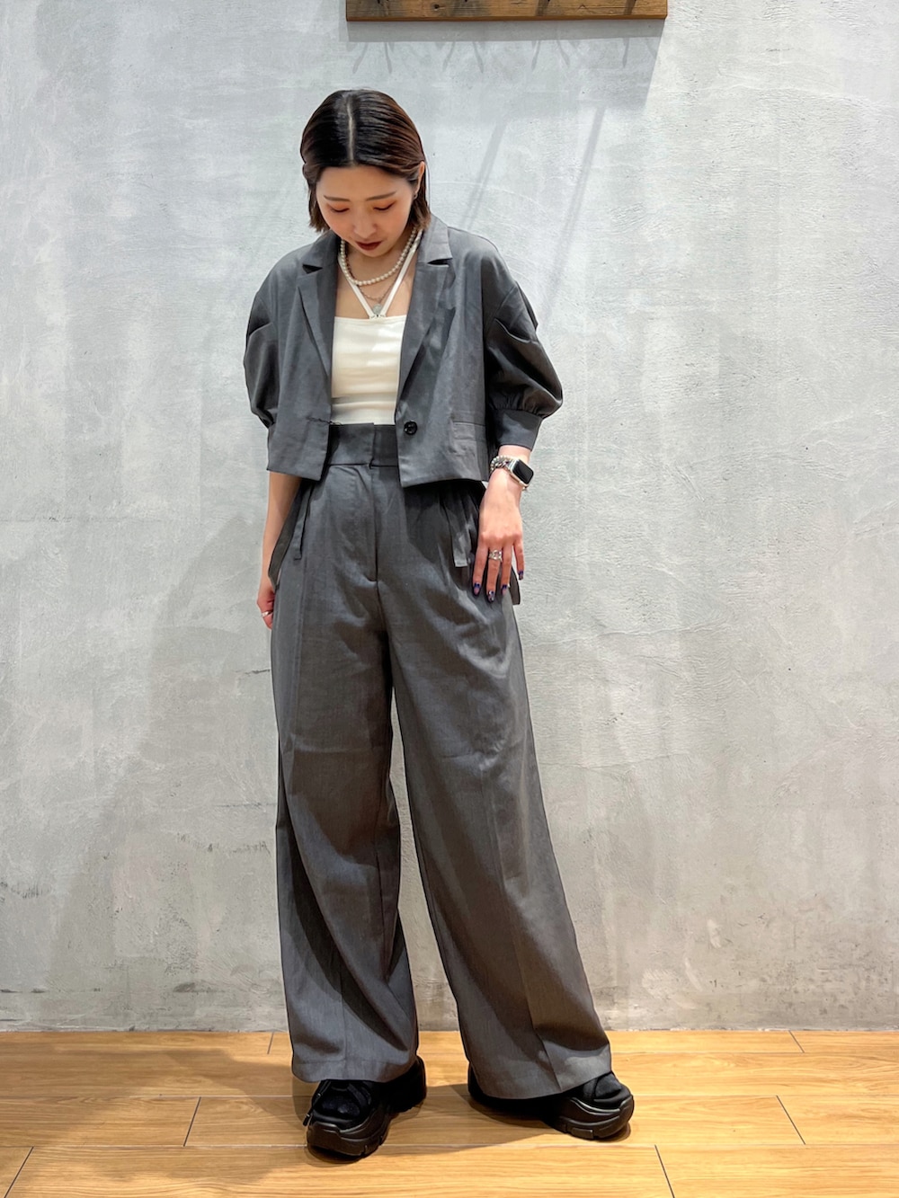 グレー系のスラックス、グレー系のテーラードジャケット、ホワイト系のキャミソールを着用したレディースの夏コーディネートの2枚目の写真