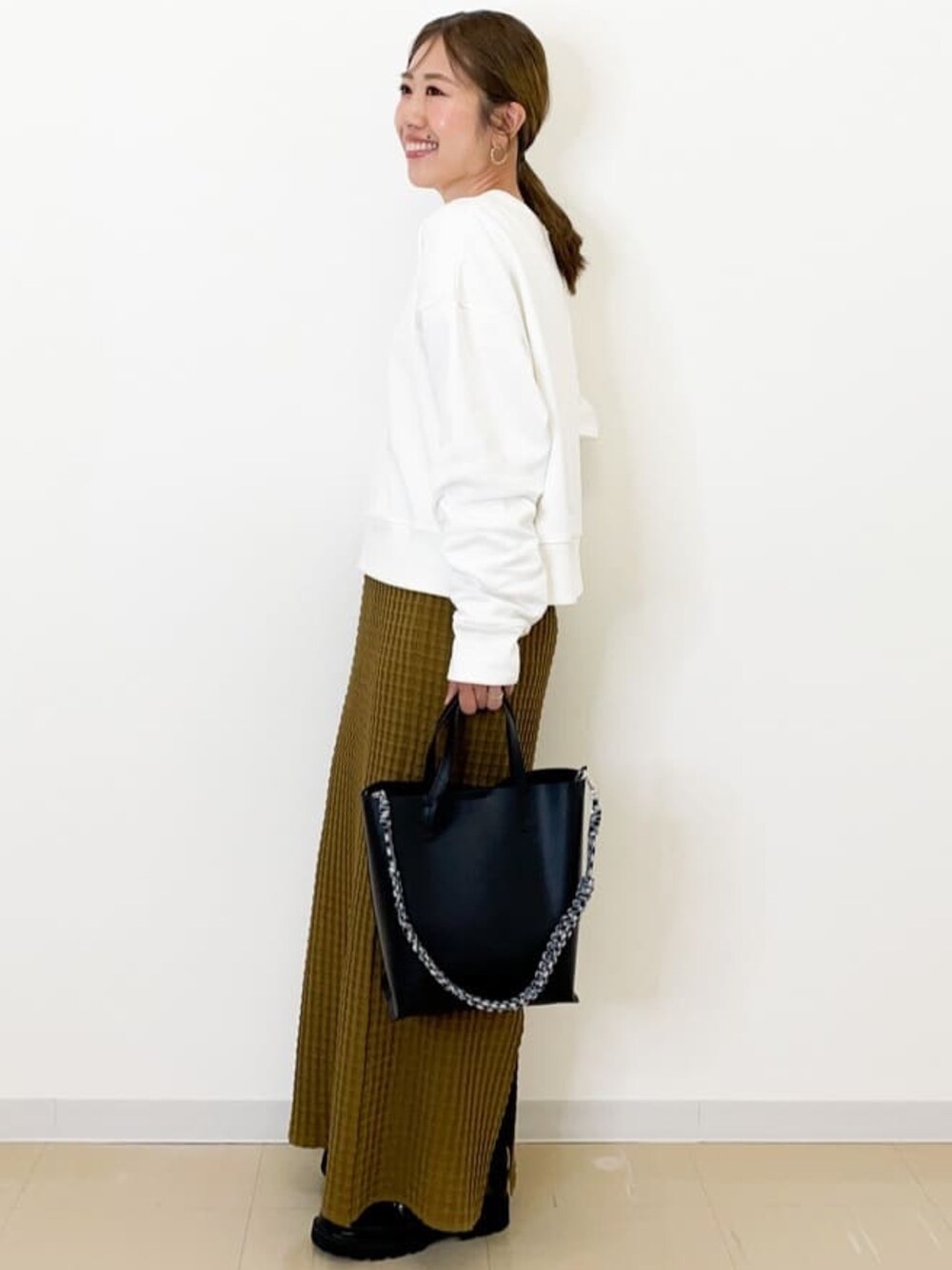 イエロー系のスカート、ブラック系のショルダーバッグ、ブラック系のパンプスを着用したレディースの秋コーディネートの3枚目の写真