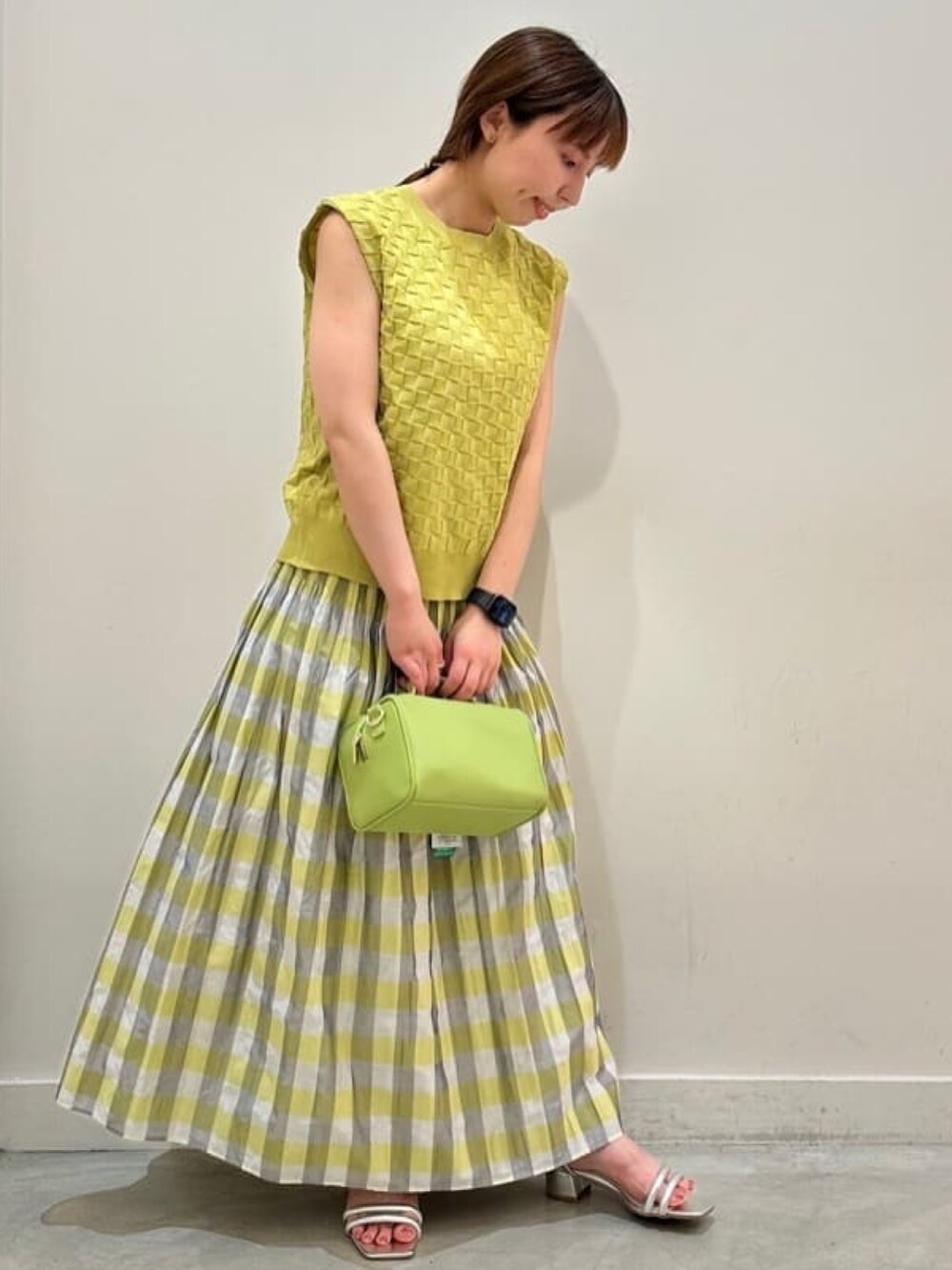 イエロー系のニット/セーター、グリーン系のボストンバッグ、イエロー系のスカートを着用したレディースの夏コーディネートの2枚目の写真
