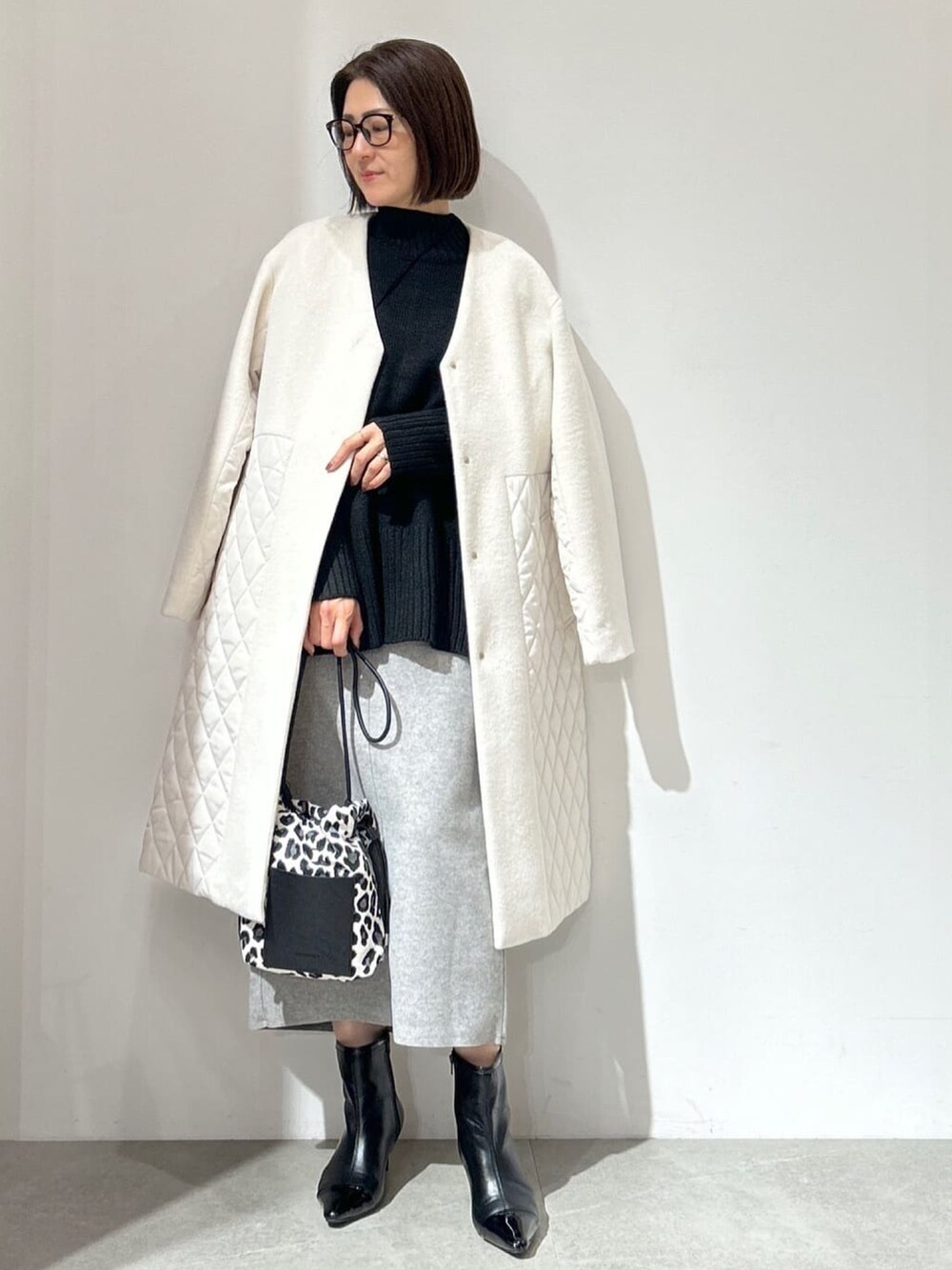 ホワイト系のノーカラーコート、グレー系のスカート、ブラック系のショルダーバッグを着用したレディースの秋コーディネートの2枚目の写真