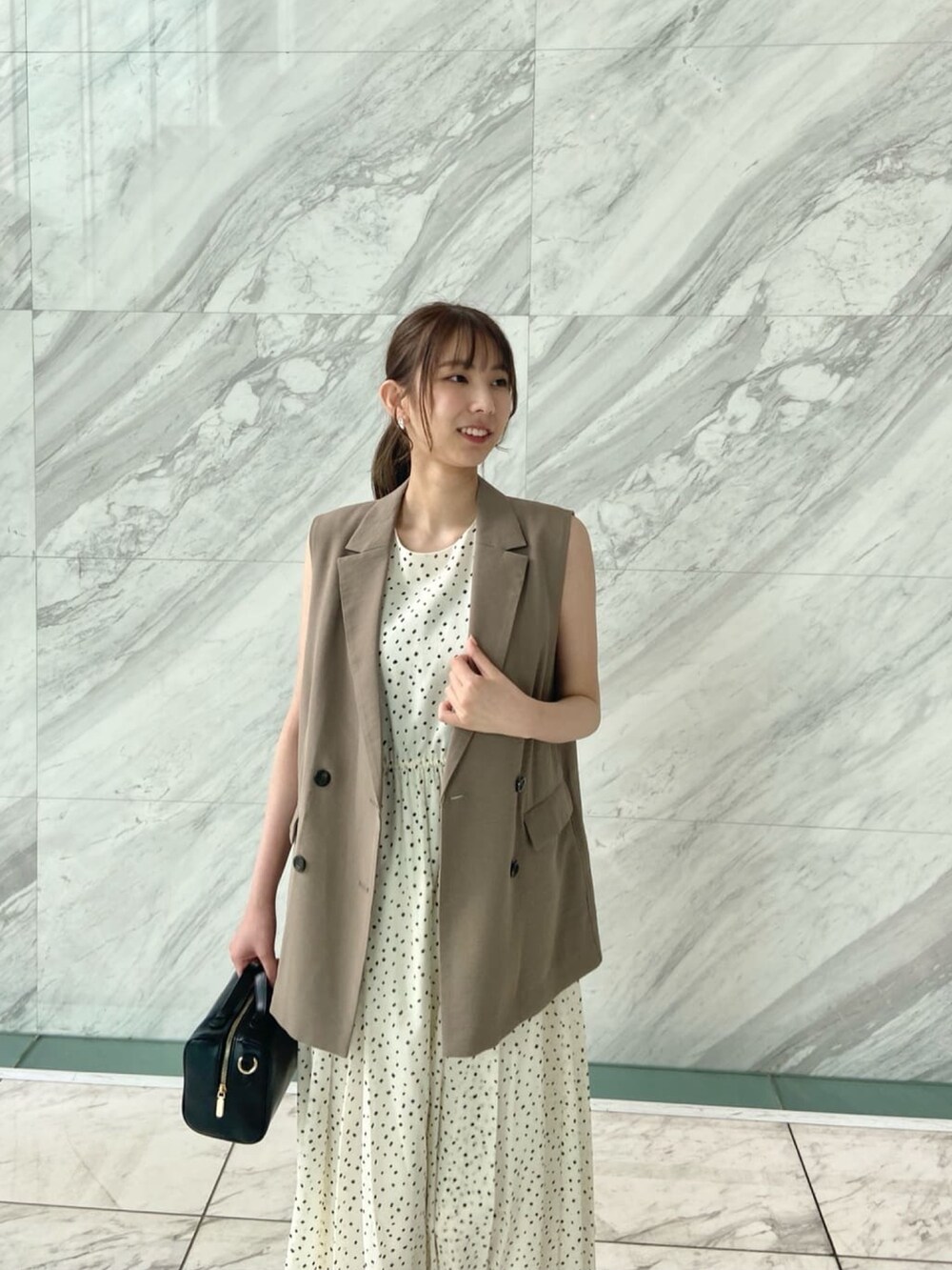 ブラウン系のベスト、ホワイト系のワンピース、ブラック系のサンダルを着用したレディースの春コーディネートの7枚目の写真