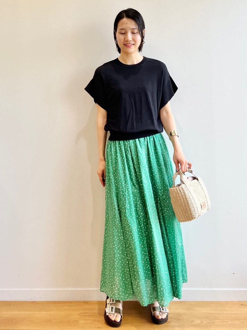 ブラック系のニット/セーター、グリーン系のスカート、ゴールド系のサンダルを着用したレディースの春コーディネートの2枚目の写真