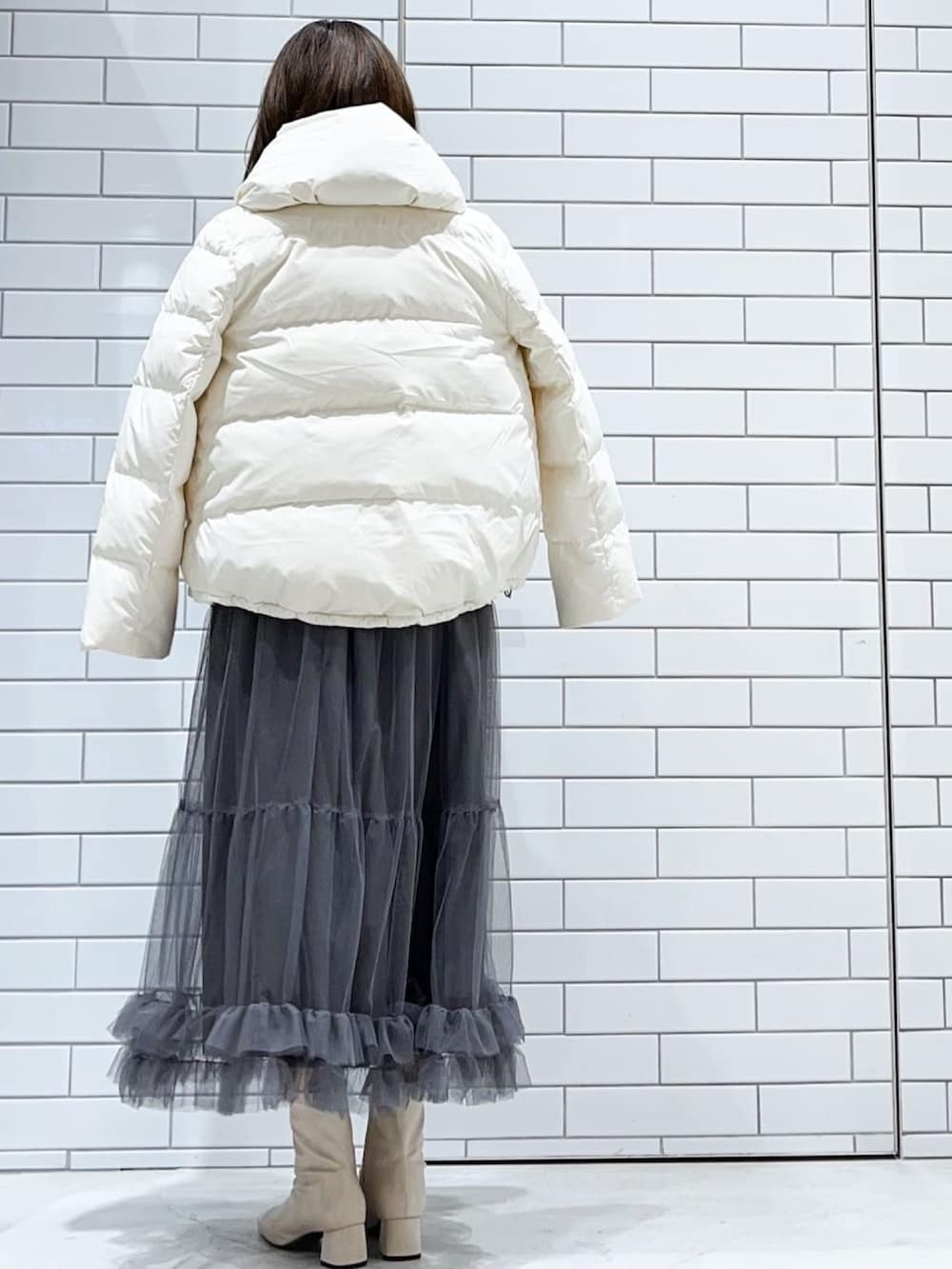 グレー系のスカート、ホワイト系のブーツ、ブラック系のショルダーバッグを着用したレディースの冬コーディネートの2枚目の写真