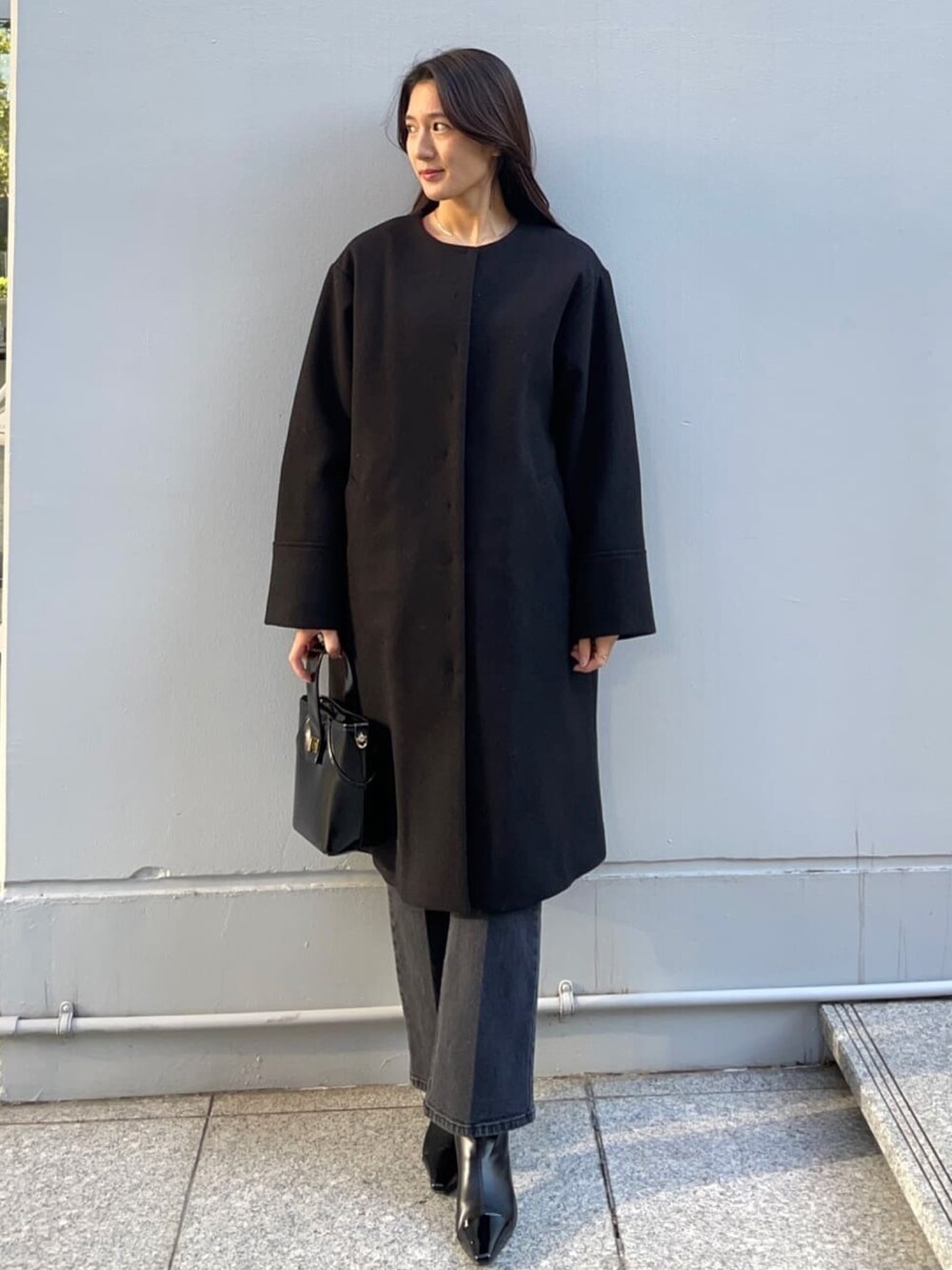 レッド系のニット/セーター、ブラック系のノーカラーコート、ブラック系のデニムパンツを着用したレディースの冬コーディネートの2枚目の写真