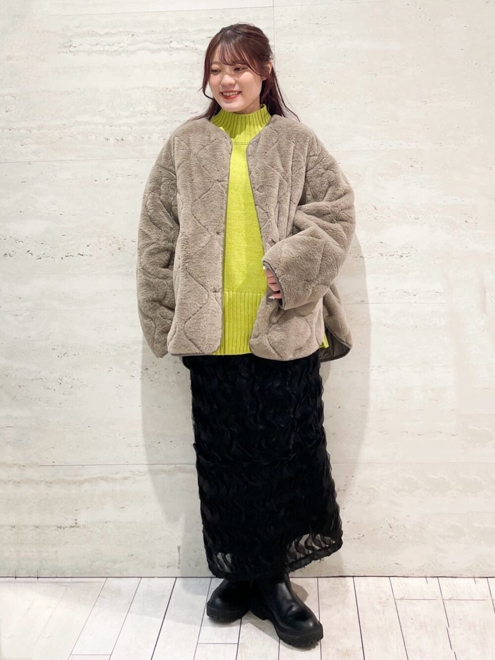 ブラウン系のノーカラーコート、イエロー系のニット/セーター、ブラック系のスカートを着用したレディースの冬コーディネートの2枚目の写真