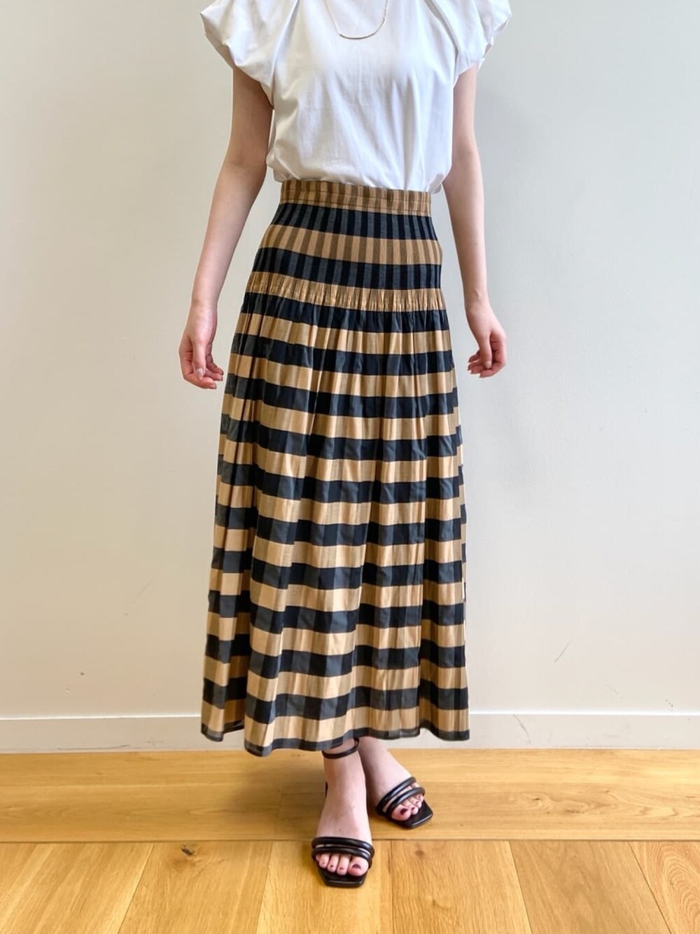 ベージュ系のスカート、ホワイト系のTシャツ/カットソー、ブラック系のサンダルを着用したレディースの夏コーディネートの9枚目の写真