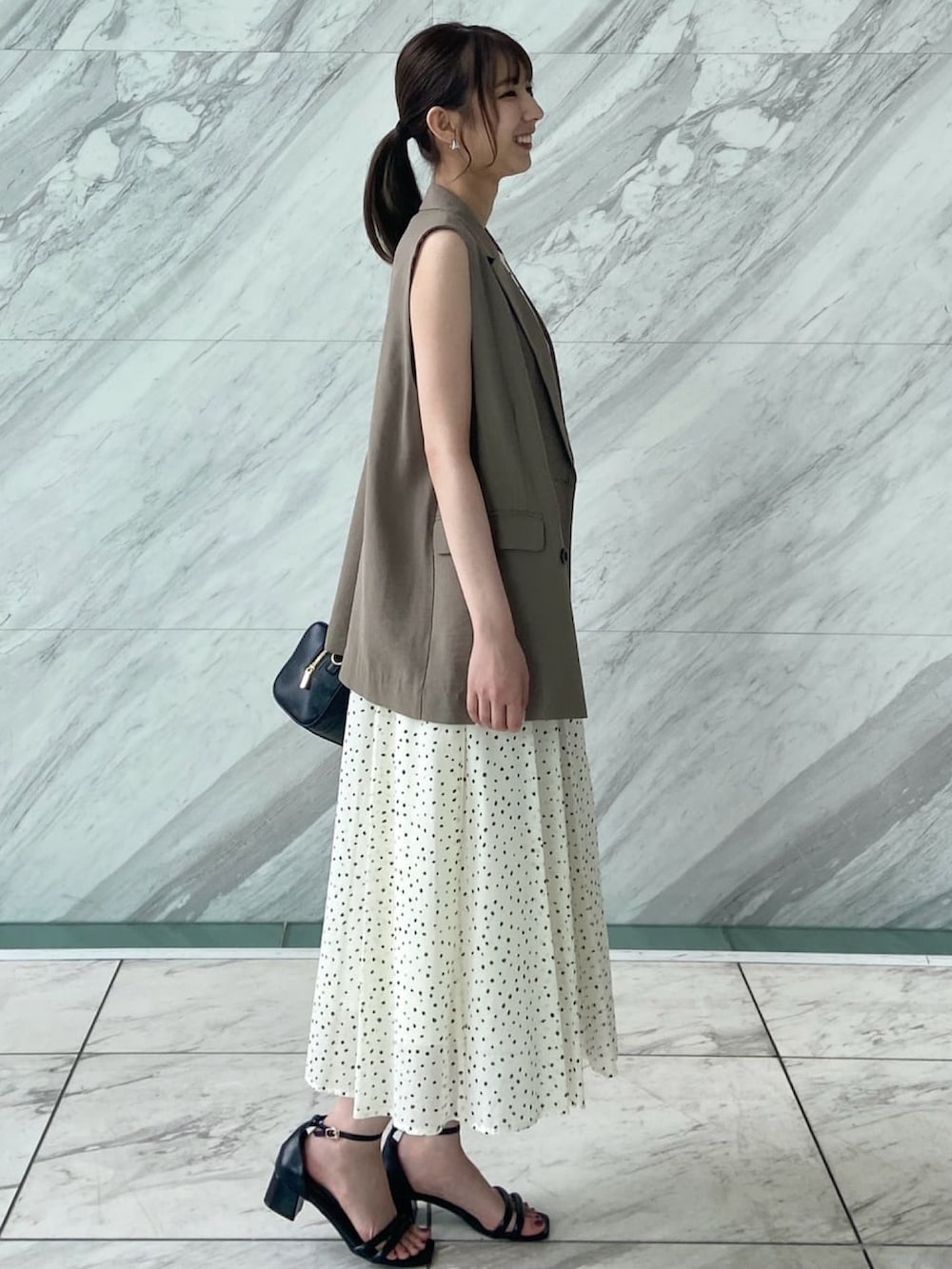 ブラウン系のベスト、ホワイト系のワンピース、ブラック系のサンダルを着用したレディースの春コーディネートの4枚目の写真