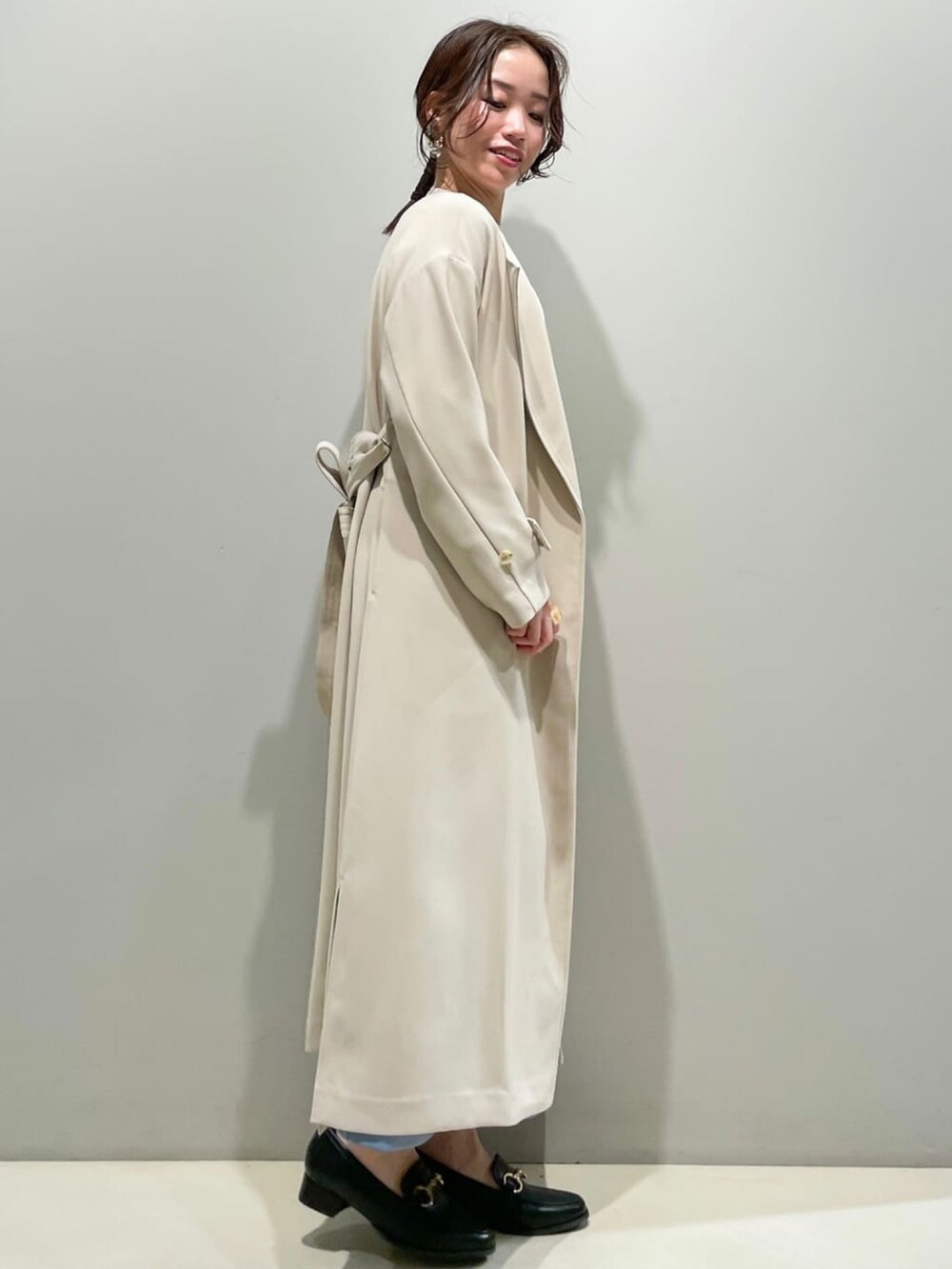 ベージュ系のステンカラーコート、ホワイト系のニット/セーター、ブルー系のスカートを着用したレディースの春コーディネートの2枚目の写真