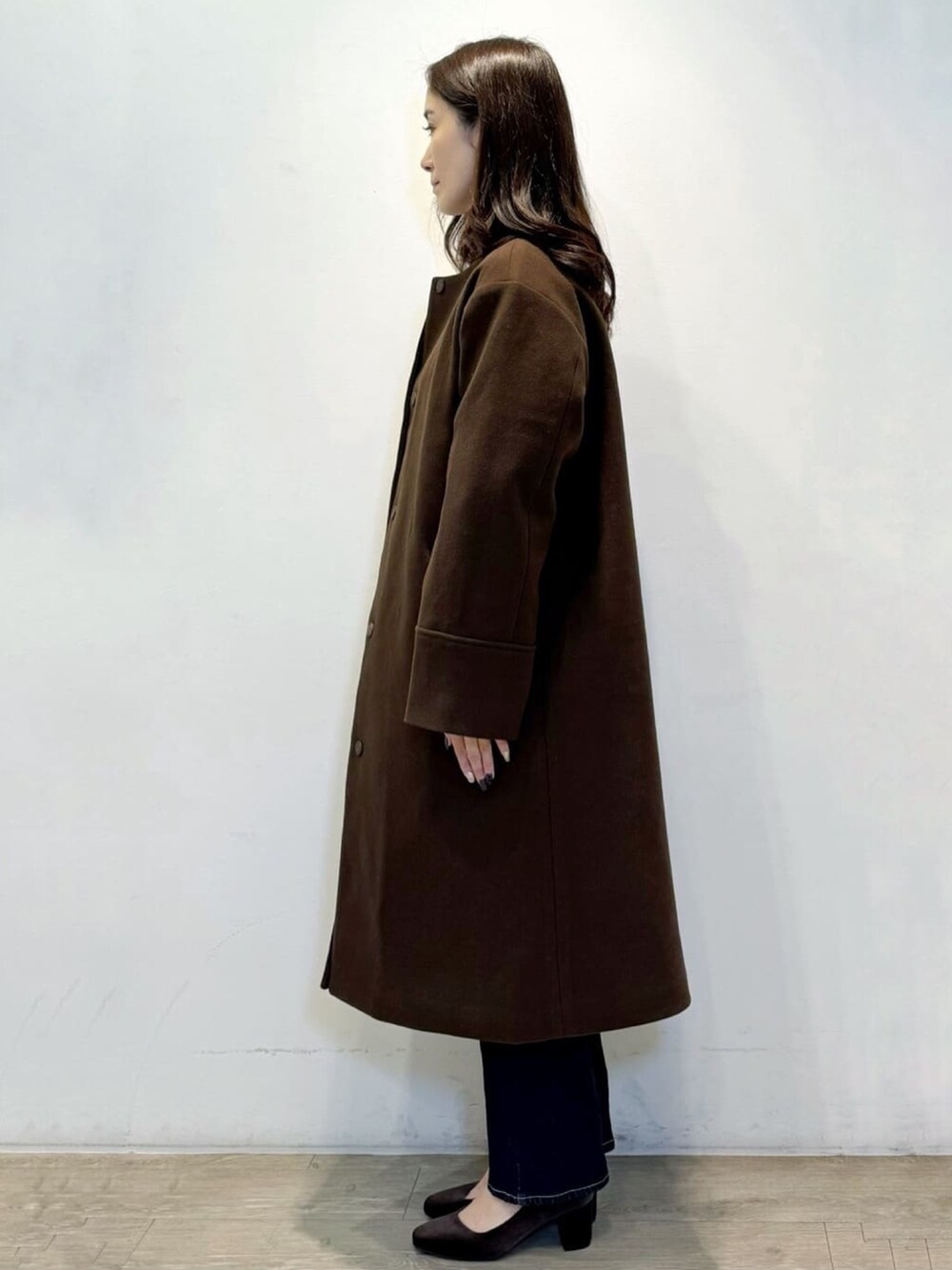 ブラウン系のノーカラーコート、ホワイト系のニット/セーター、ブルー系のデニムパンツを着用したレディースの冬コーディネートの3枚目の写真