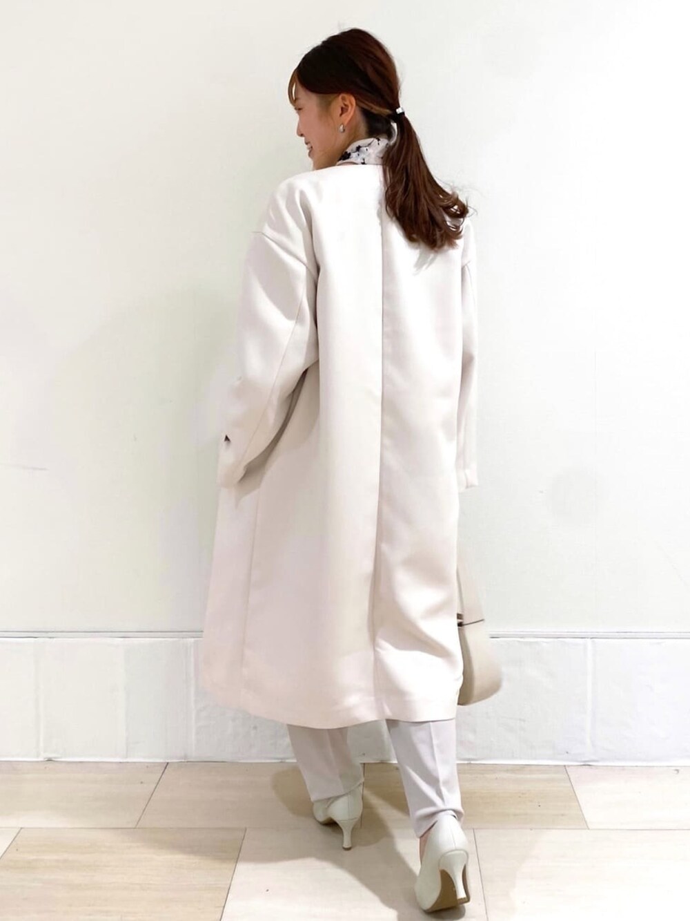 ホワイト系のノーカラーコート、グリーン系のニット/セーター、ホワイト系のパンプスを着用したレディースの冬コーディネートの2枚目の写真