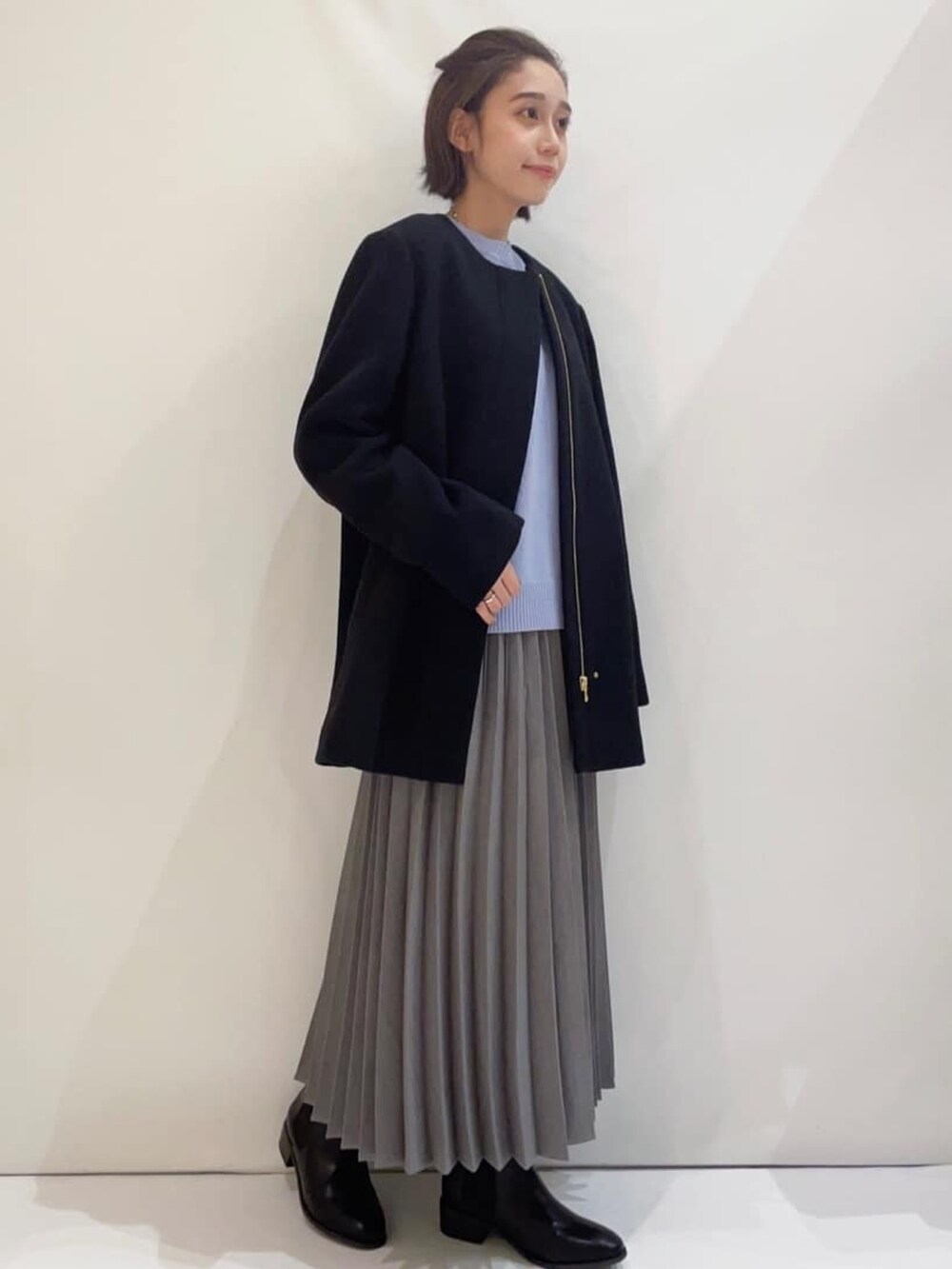 ブラック系のノーカラーコート、ブルー系のニット/セーター、グレー系のスカートを着用したレディースの冬コーディネートの2枚目の写真