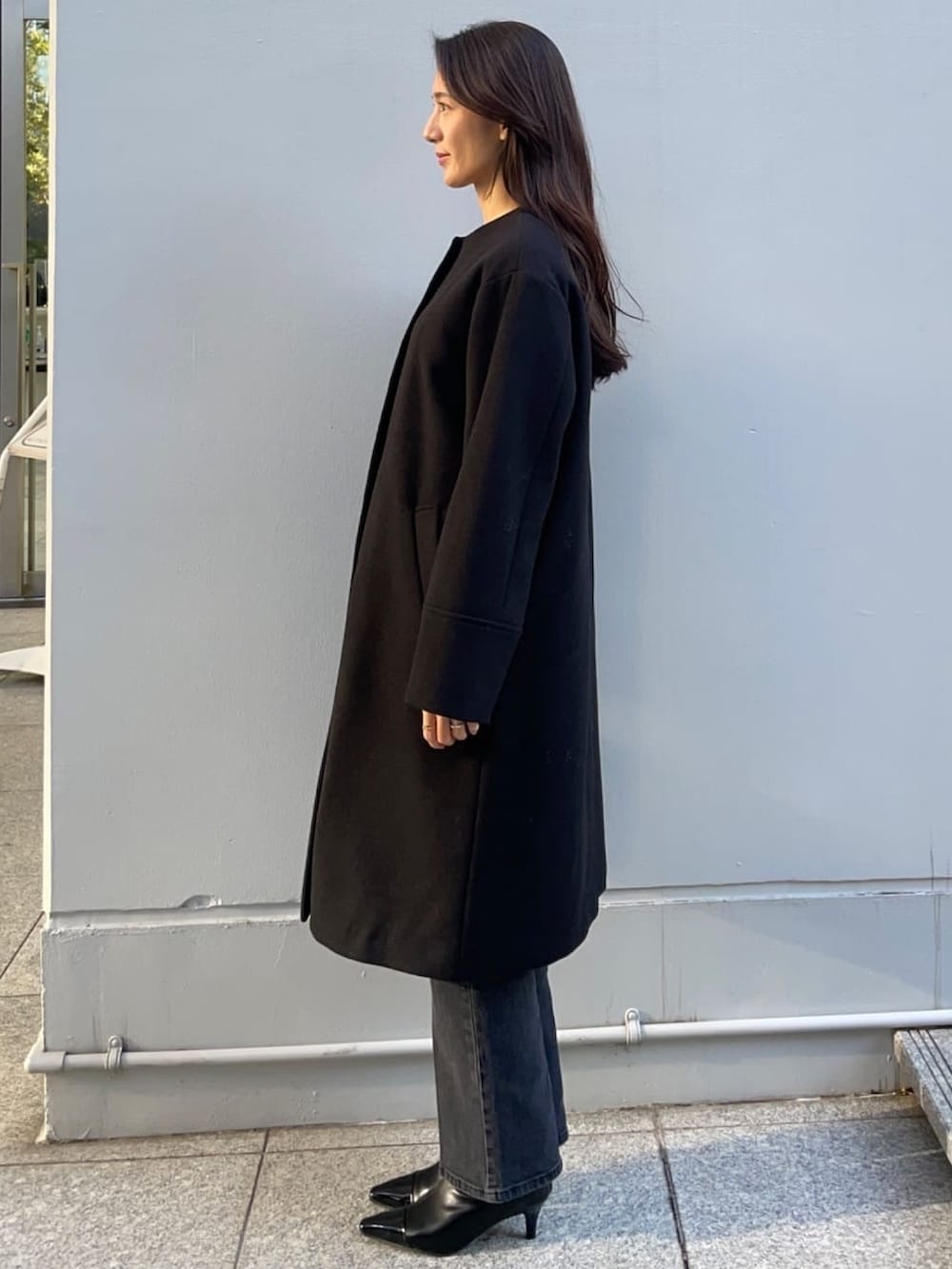 レッド系のニット/セーター、ブラック系のノーカラーコート、ブラック系のデニムパンツを着用したレディースの冬コーディネートの3枚目の写真