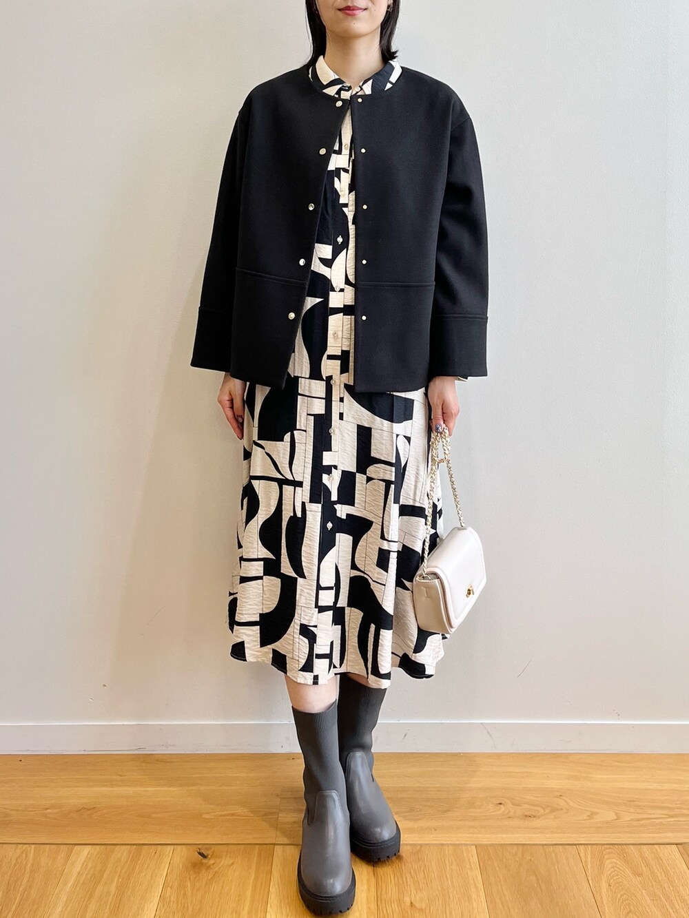 ブラック系のノーカラーコート、ベージュ系のワンピース、ブラック系のブーツを着用したレディースの秋コーディネートの4枚目の写真