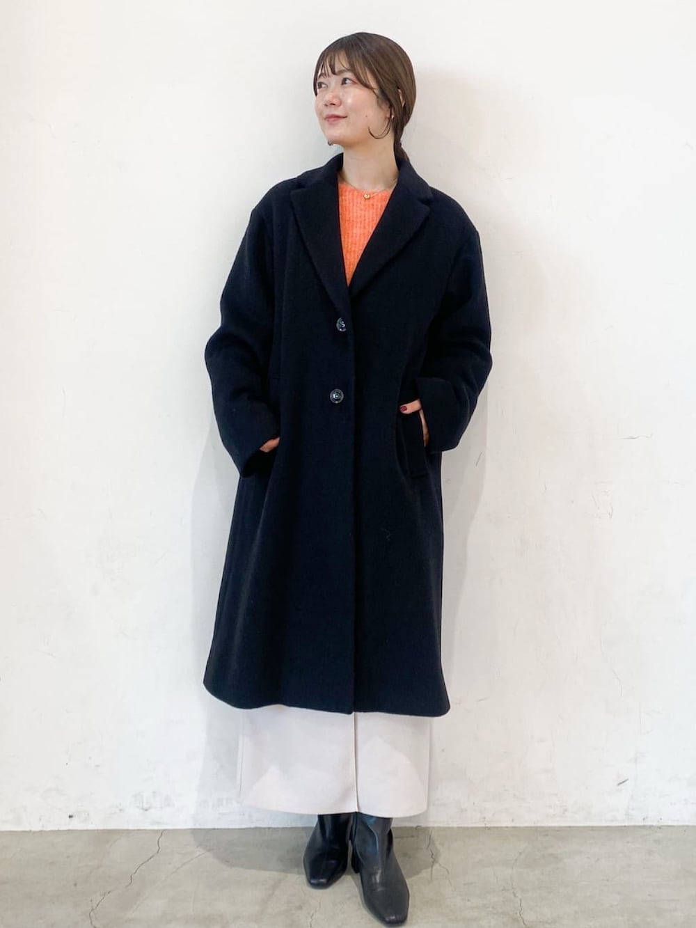 ブラック系のチェスターコート、オレンジ系のニット/セーター、ベージュ系のスカートを着用したレディースの冬コーディネートの2枚目の写真