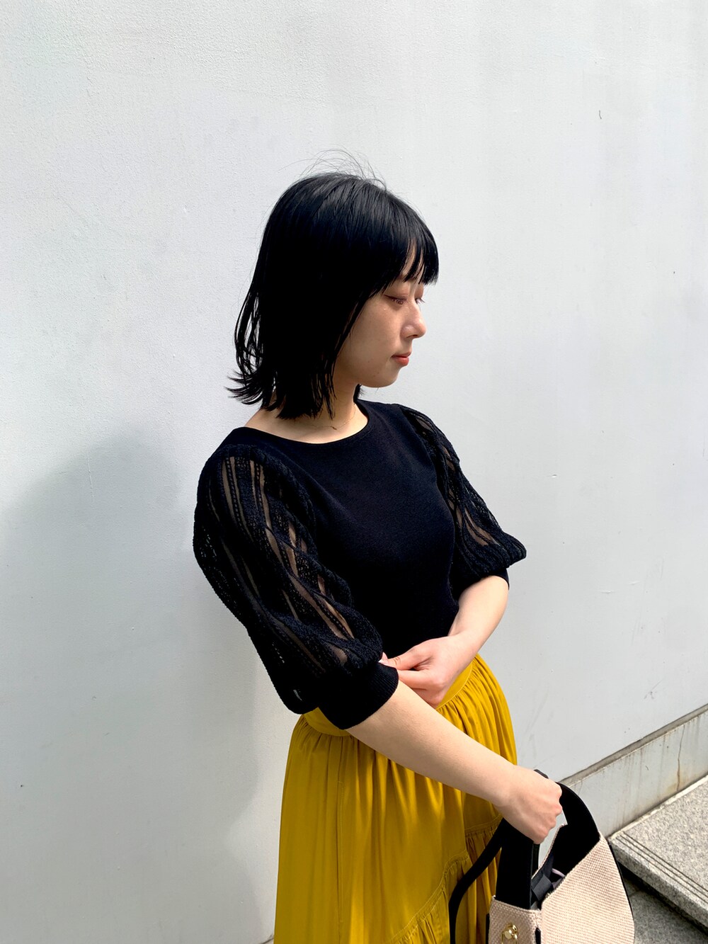 ブラック系のニット/セーター、イエロー系のスカート、ブラック系のショルダーバッグを着用したレディースの春コーディネートの2枚目の写真